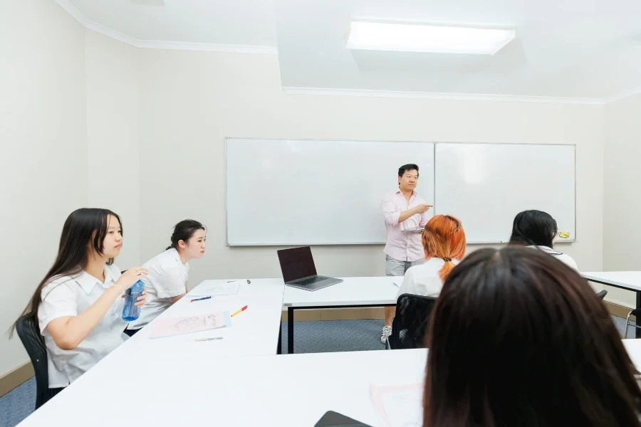 A classroom with students sitting at desks and a teacher standing at the front near a whiteboard.