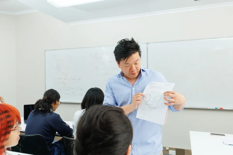 A teacher reviewing a diagram with students in a classroom with a whiteboard in the background.