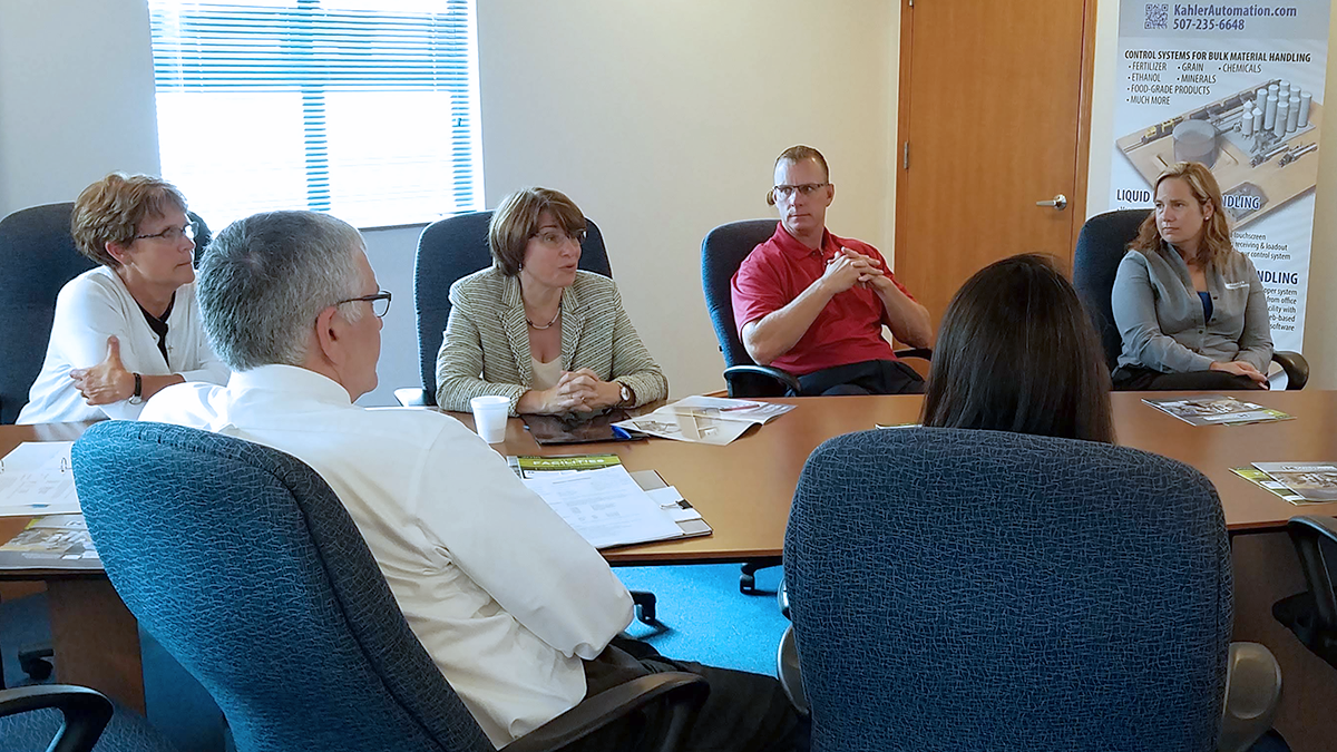 Sen. Klobuchar asks for details on Kahler Automation’s history, as Fairmont Mayor Debbie Foster (left) and others listen on.