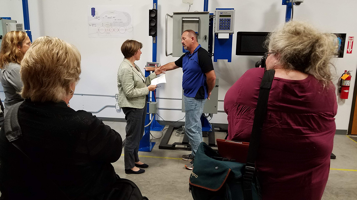 Sen. Klobuchar asks Paul Rehm for examples of applications for Kahler’s truck traffic control system, as local media document the Senator’s visit.