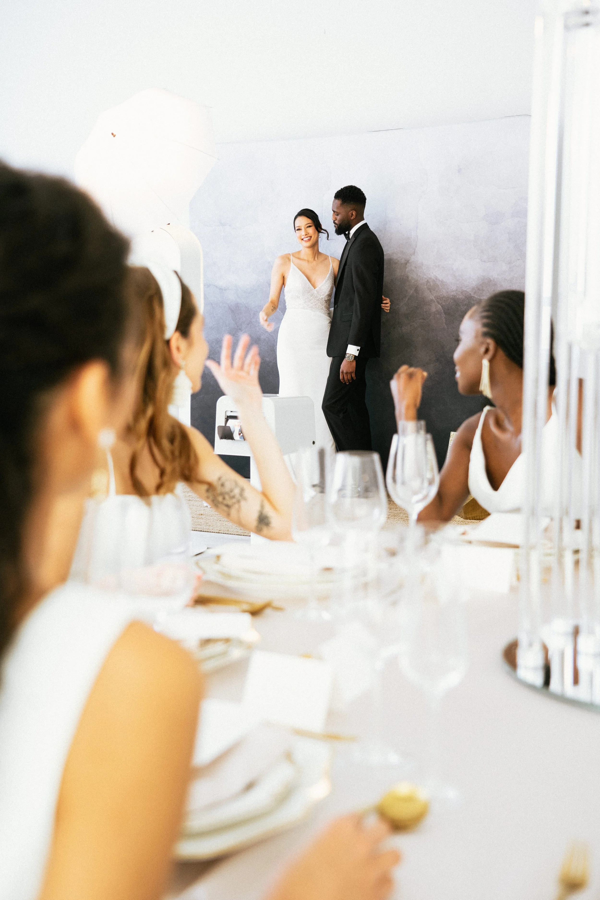 A bride and groom posing on a stage during their wedding reception while guests watch from a decorated table.