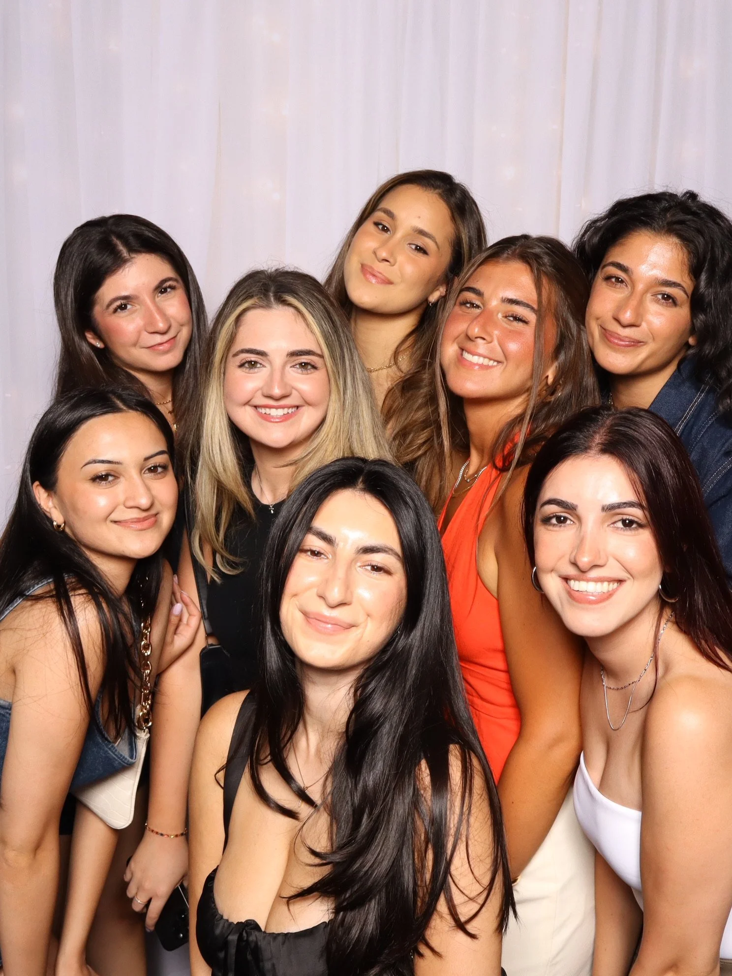 Group of ten young women smiling and posing together in front of a light-colored backdrop.