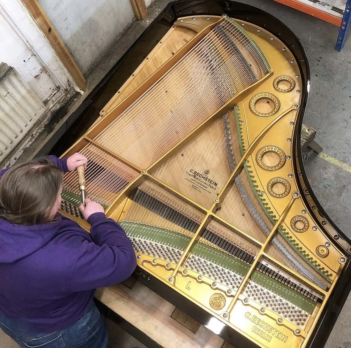A person tuning a grand piano showing the inside of the piano