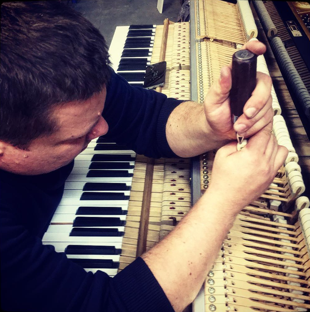 Picture of a piano technician working on the hammers or dampers of a piano