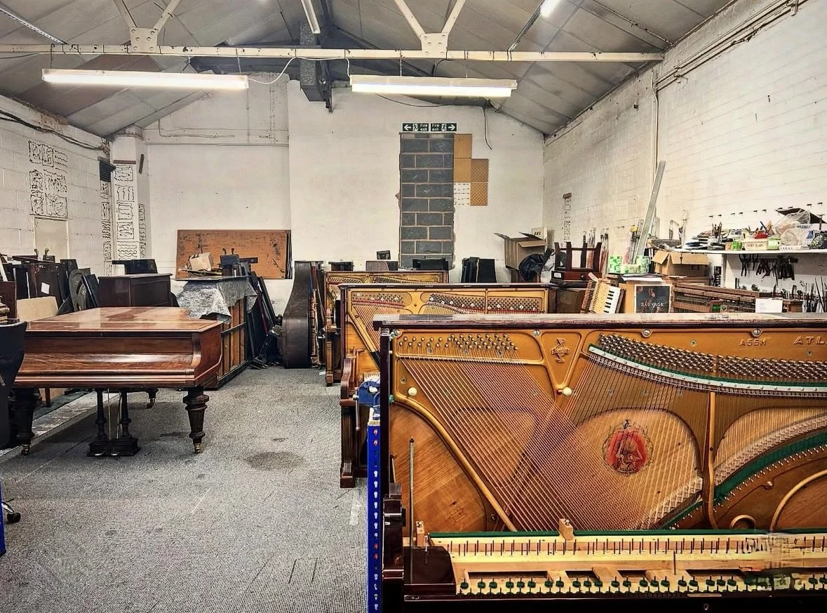 Picture of a piano workshop showing multiple upright pianos and a grand piano being worked on