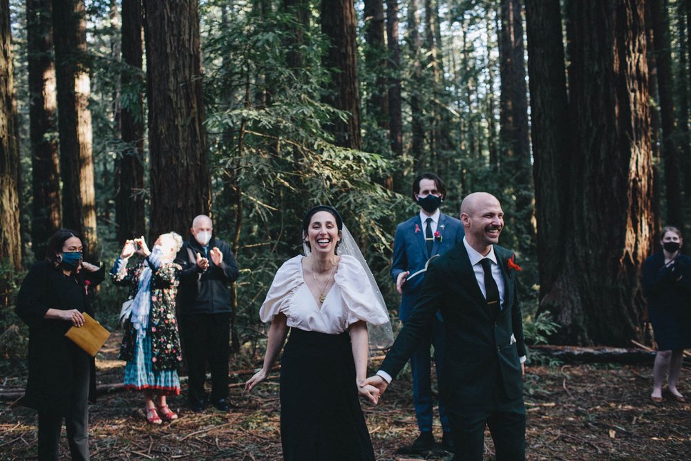 a joyful couple just married in a ceremony in a redwood grove at joaquin miller park in oakland