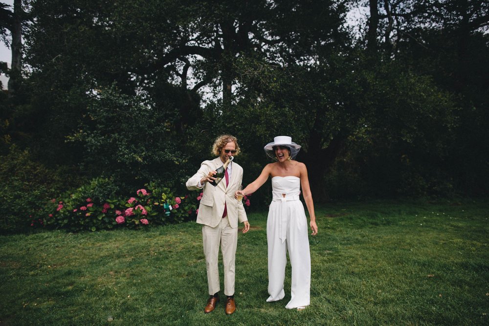 a bride wears a gorgeous two piece pantsuit as she celebrates with champagne on her wedding day