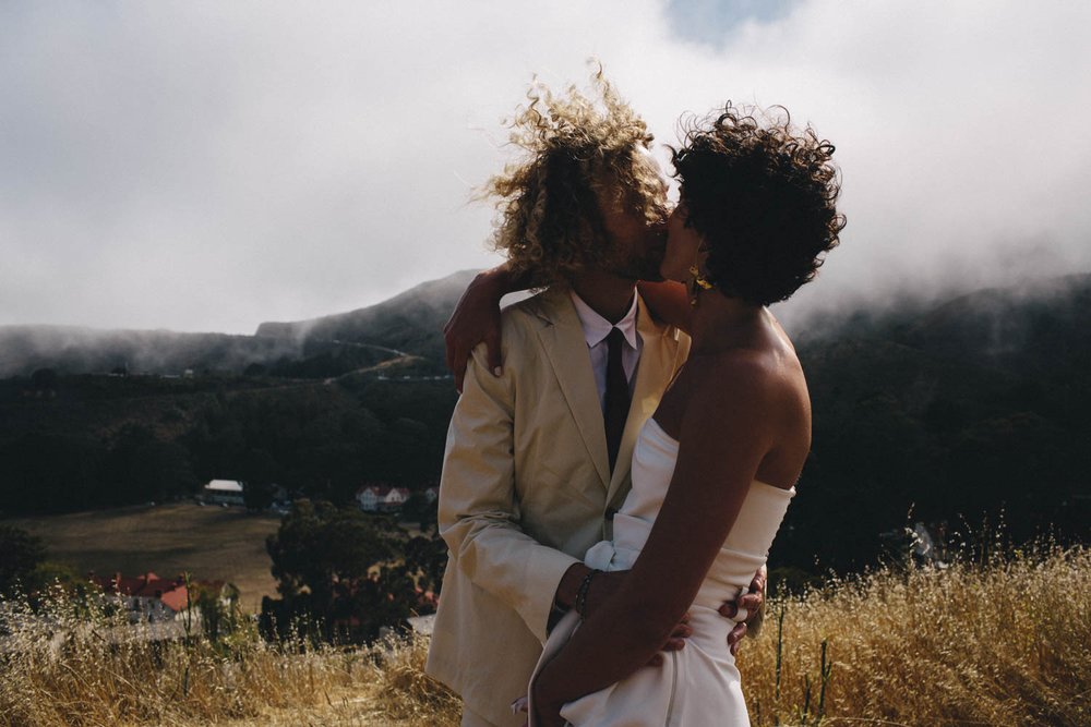 a couple kissing on their wedding day with san francisco fog rolling over the mountains in the background