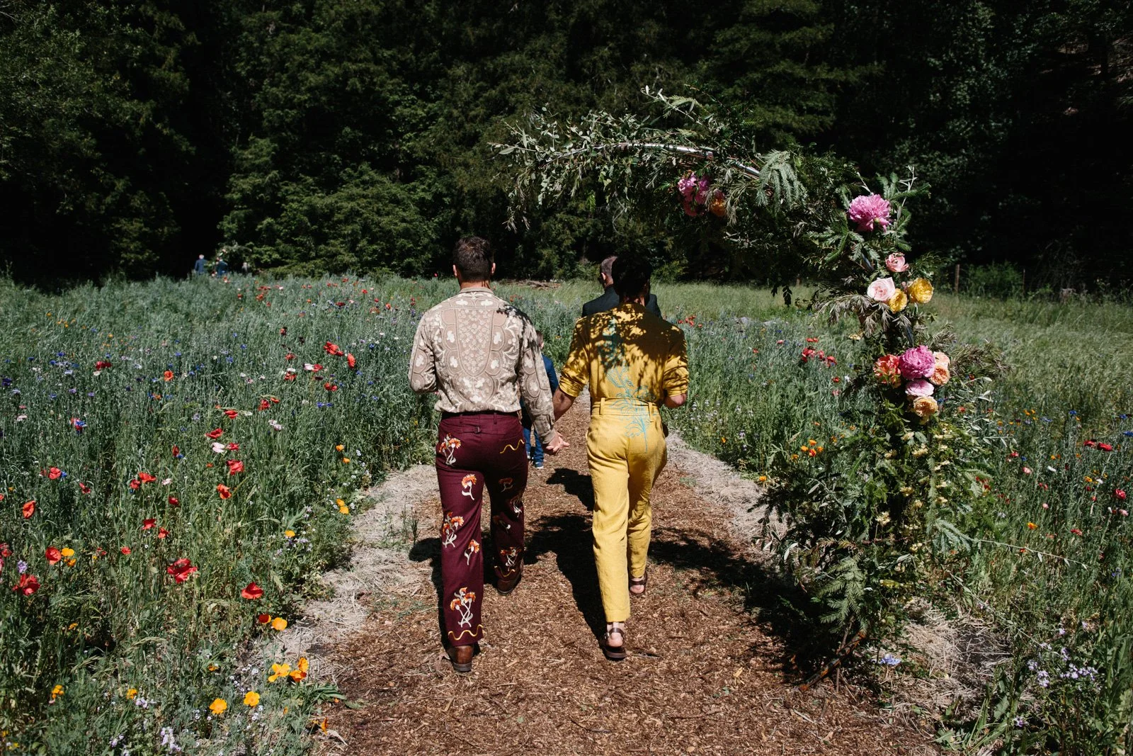 Grooms walk to their wedding ceremony through a field of wildflowers at Solar Punk Farms