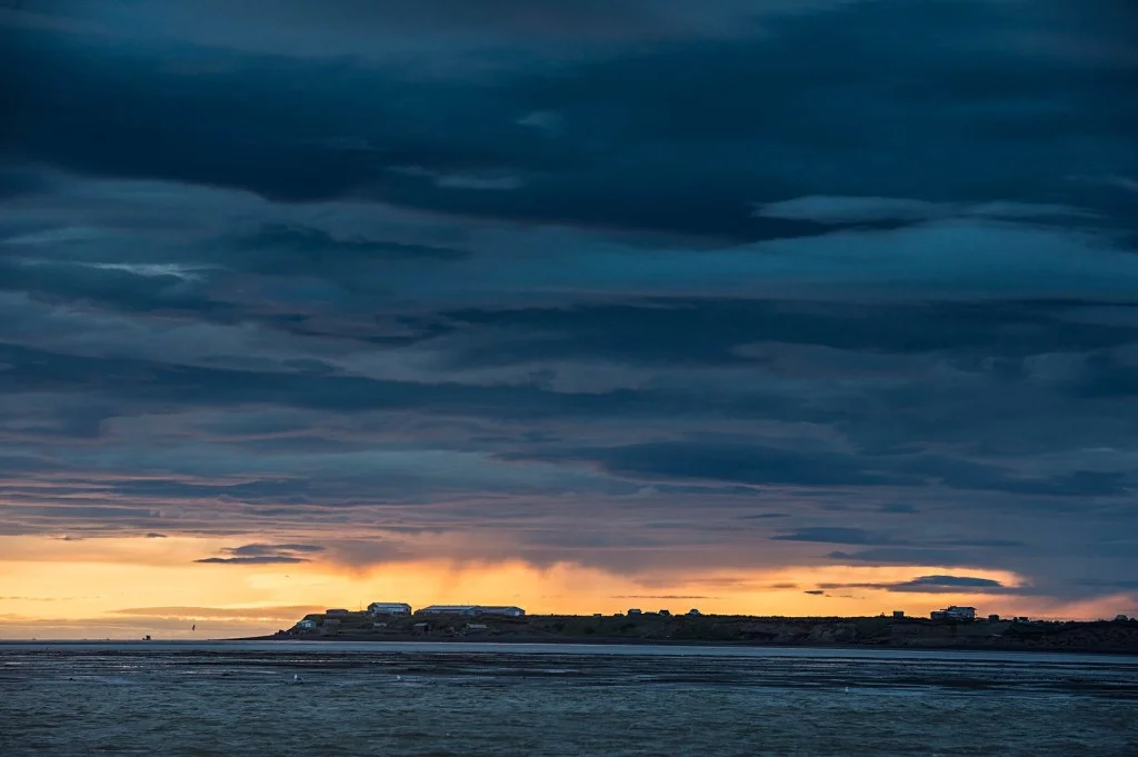 The sun sets over Coffee Point on the bank of the Egegik River as a brief shower moves through. To the left of the point in this photo is the major anchorage in the Egegik district, where the majority of the fleet “drops the hook” between openings. This entire area is intertidal, as you can see from the wide exposed mudflats stretching out to the main river channel.