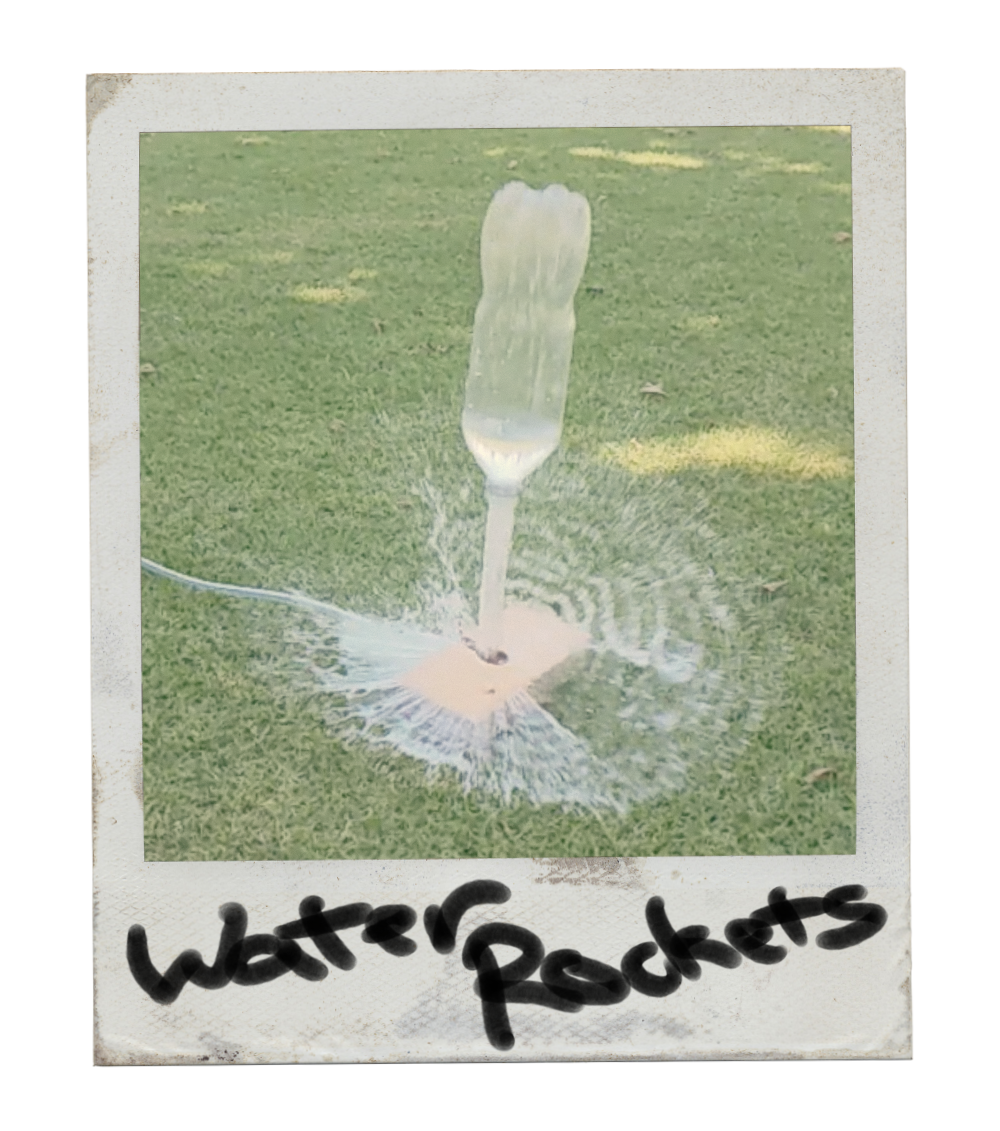 A water rocket in mid-launch, with water flying out of its base and creating a splash on the grass, labeled 'Water Rockets' on the bottom of the photo.