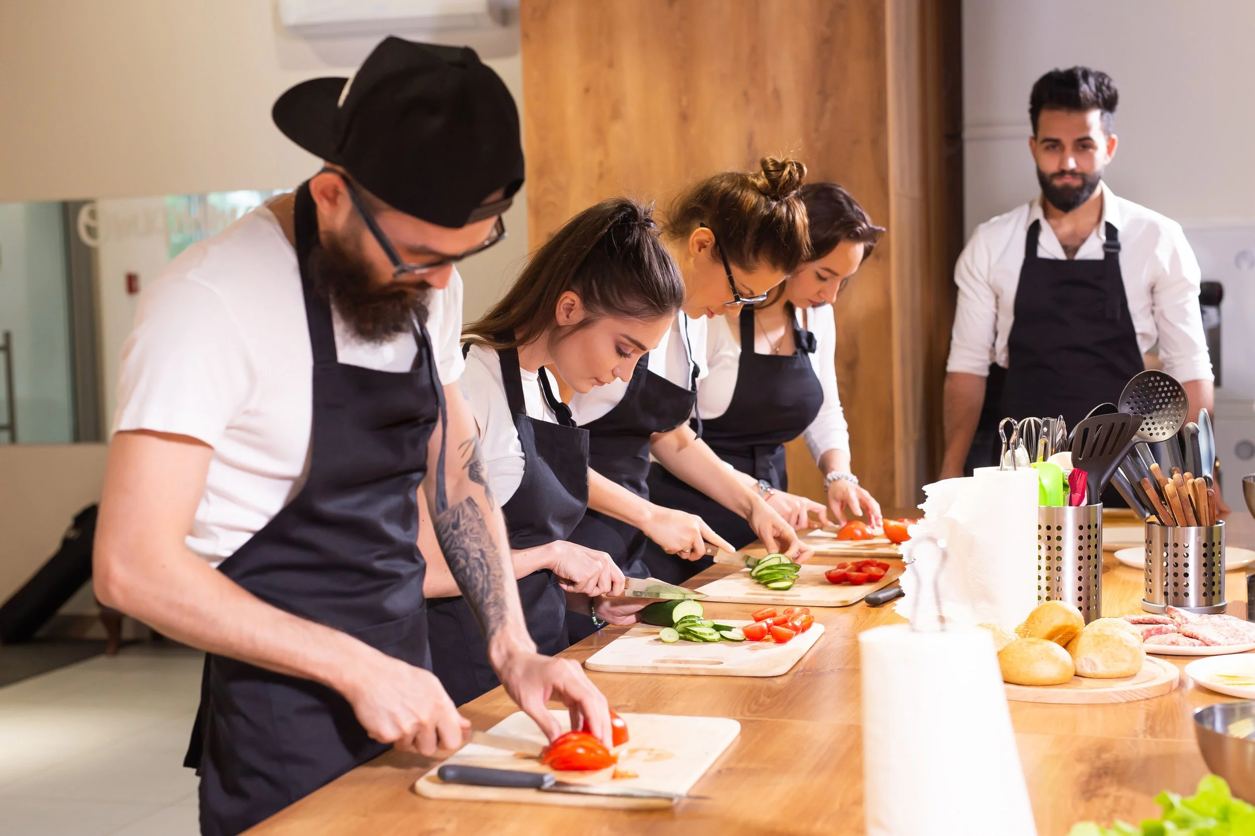 Four guests and one chef in black aprons chopping vegetables on cutting boards in a fun exclusive yet relaxed private cooking class.