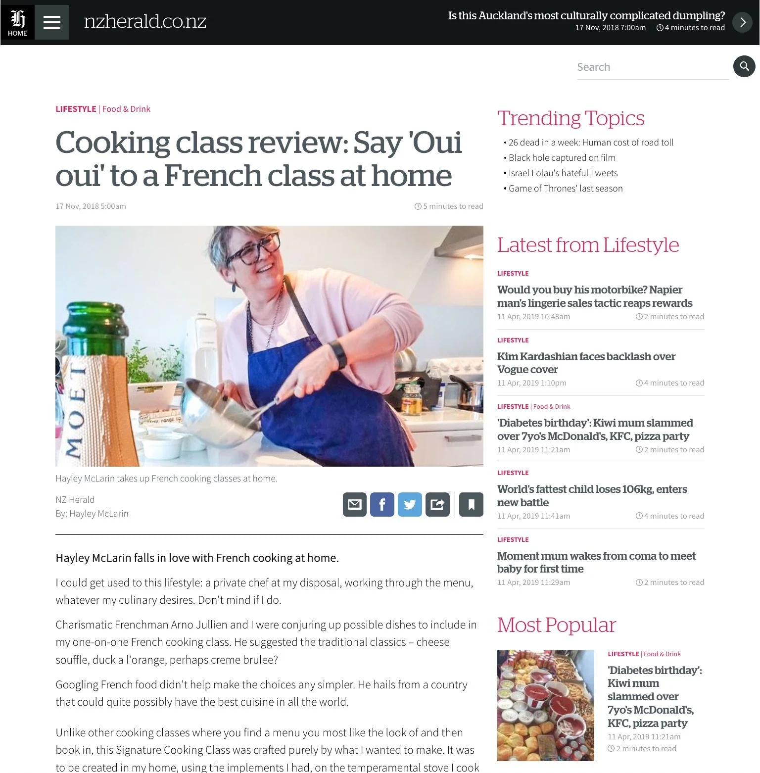 Article discussing a French cooking class at home with a featured image of a smiling person in an apron holding a bowl and a whisk, beside a bottle of Moët champagne. The page includes lifestyle news updates.