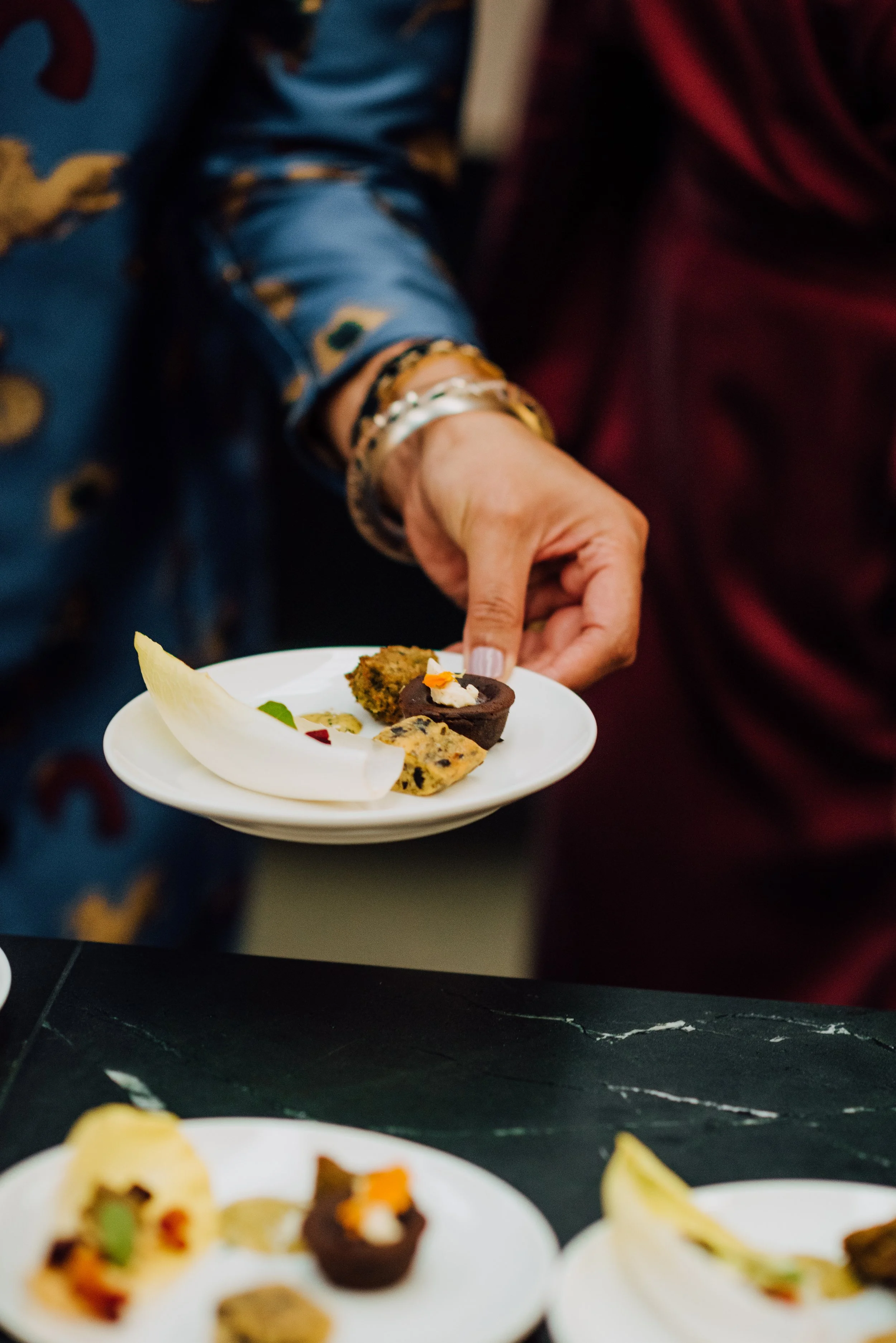 Person holding a plate with assorted appetizers, including endive leaves and gourmet bites.