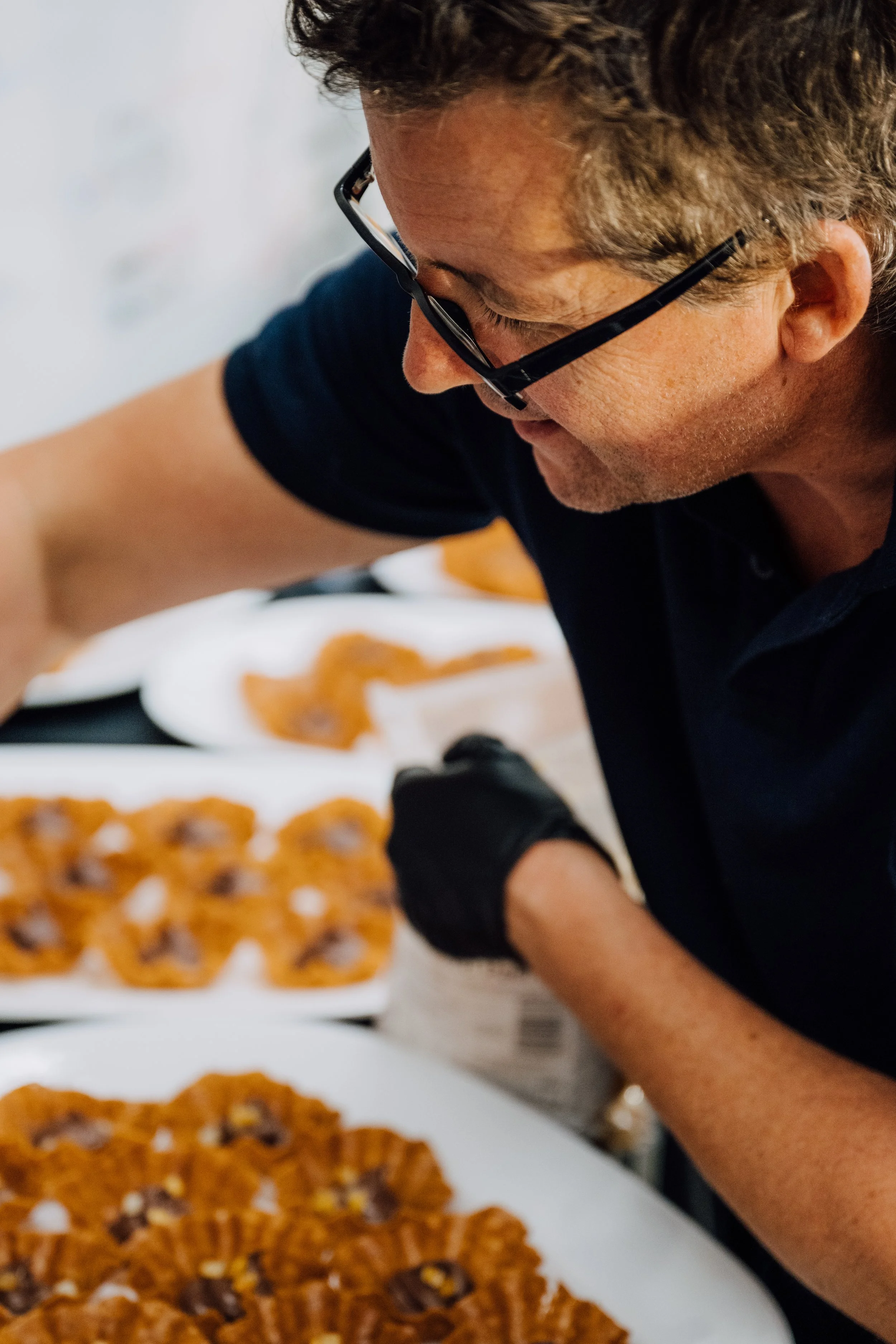 Person wearing glasses and black gloves arranging pastries on white plates.