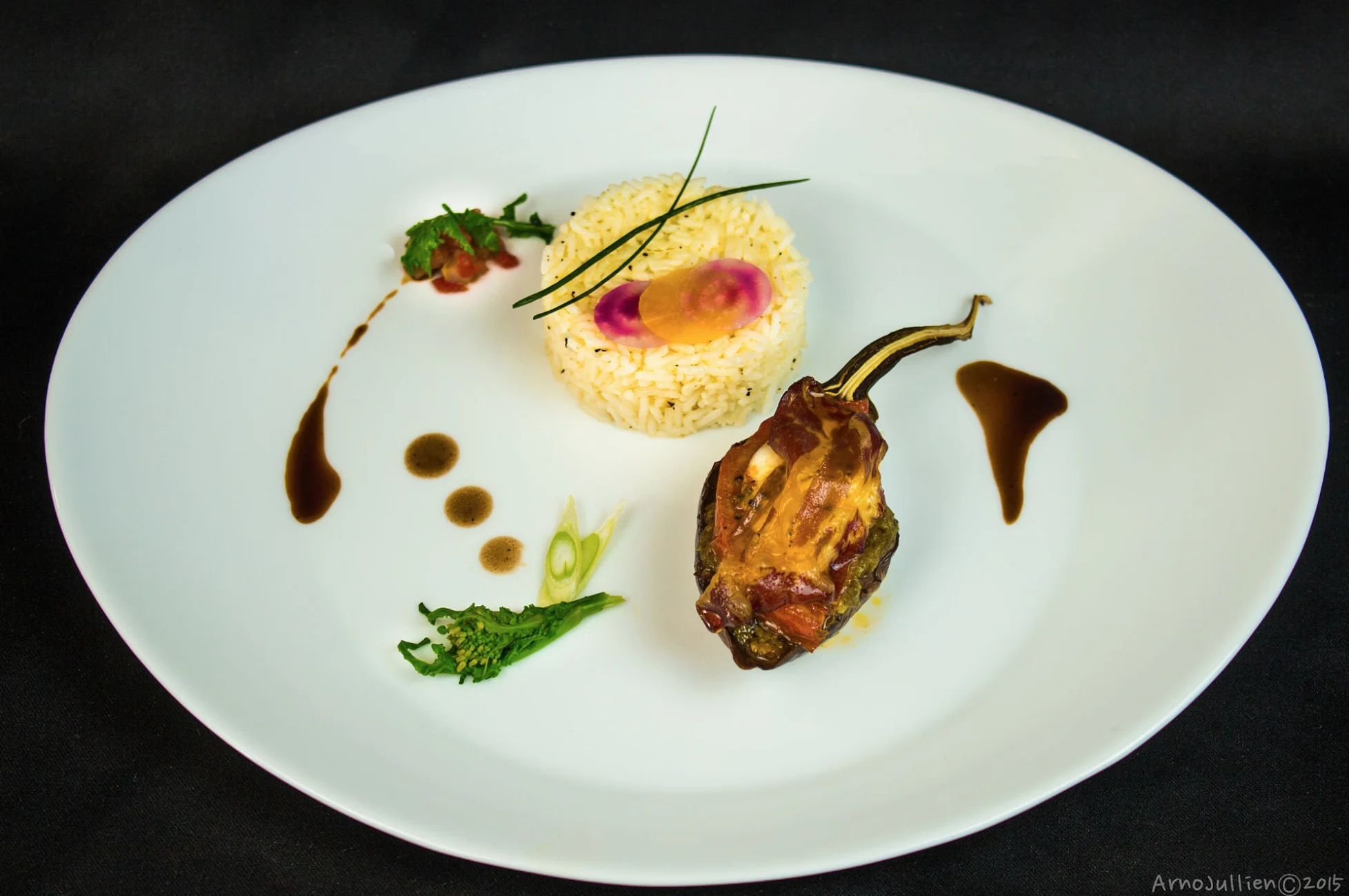 Plated dish with rice, stuffed pepper, sauces, and garnishes on a white plate.