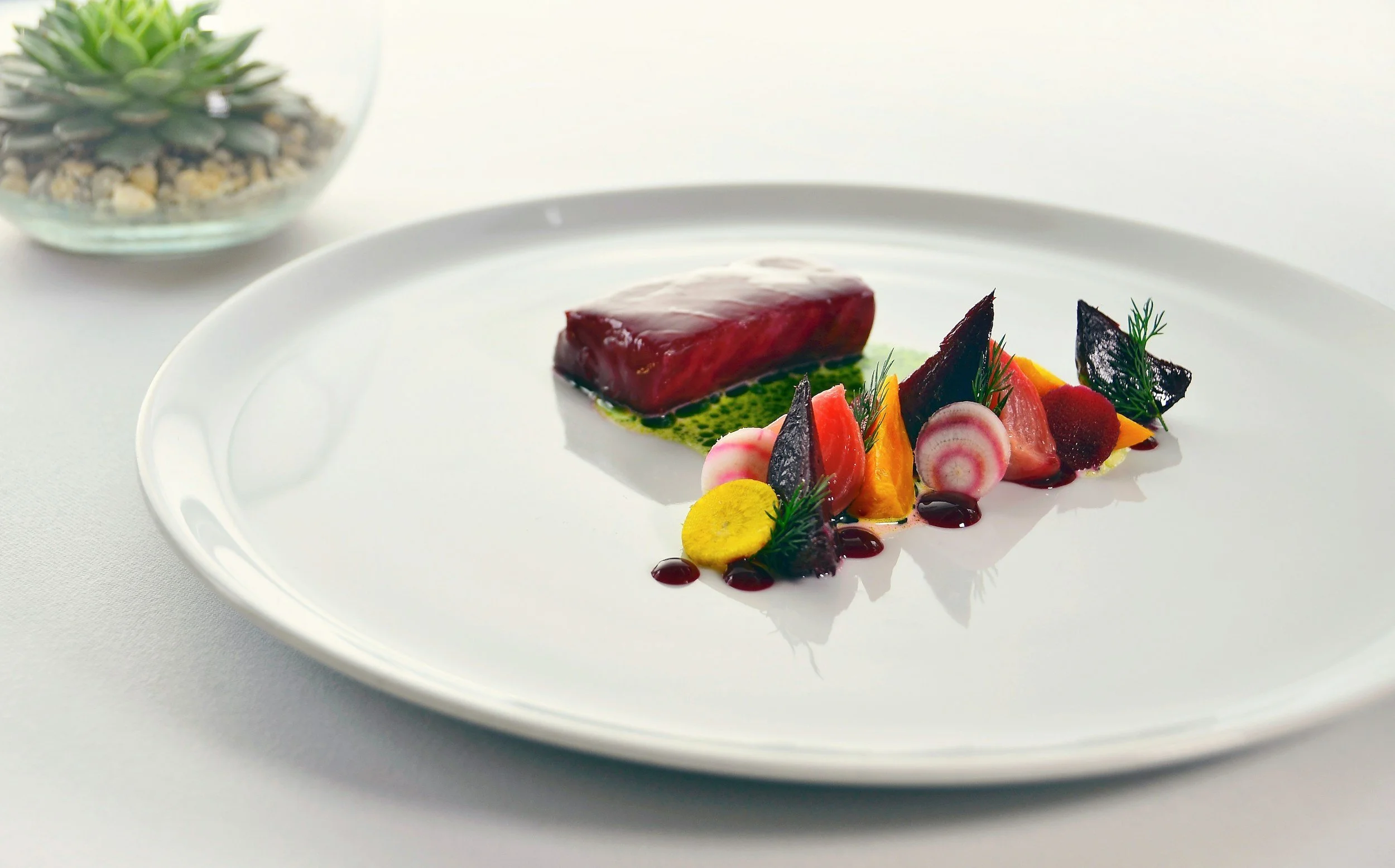 Elegant plated dish with a glazed tuna steak, colorful vegetable garnishes, and sauce on a white plate.