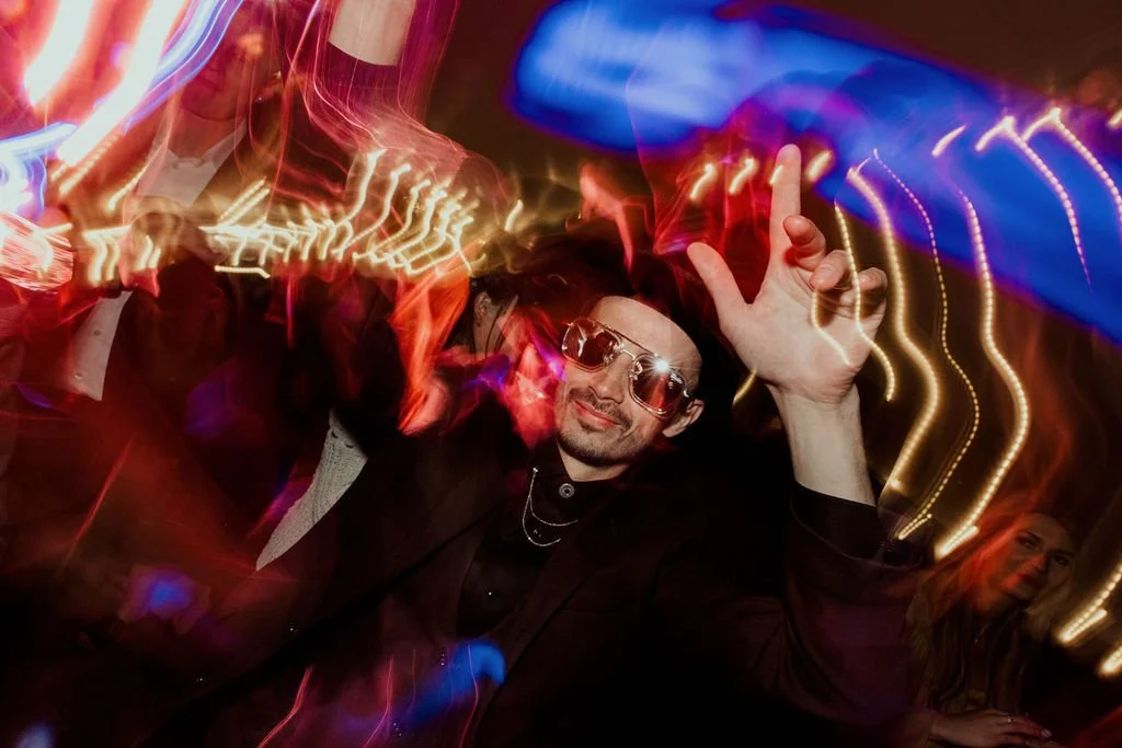 Person dancing with sunglasses at a party, colorful light trails.