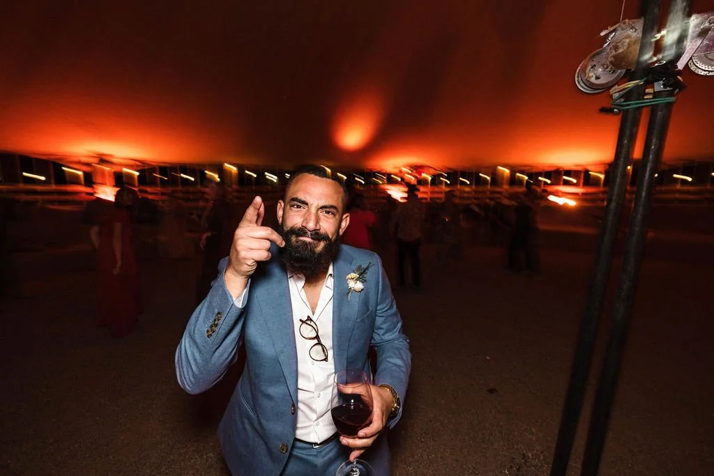Bearded man in blue suit holding a drink at a party under warm lighting.