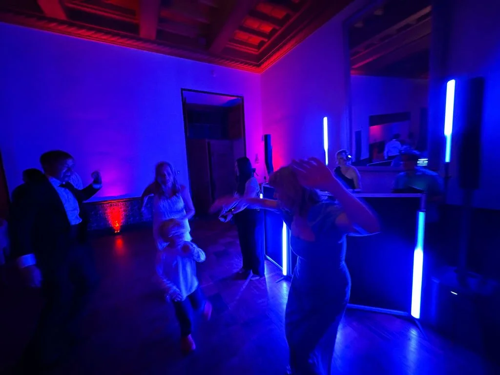 People dancing at a party with colorful lights and a DJ booth.