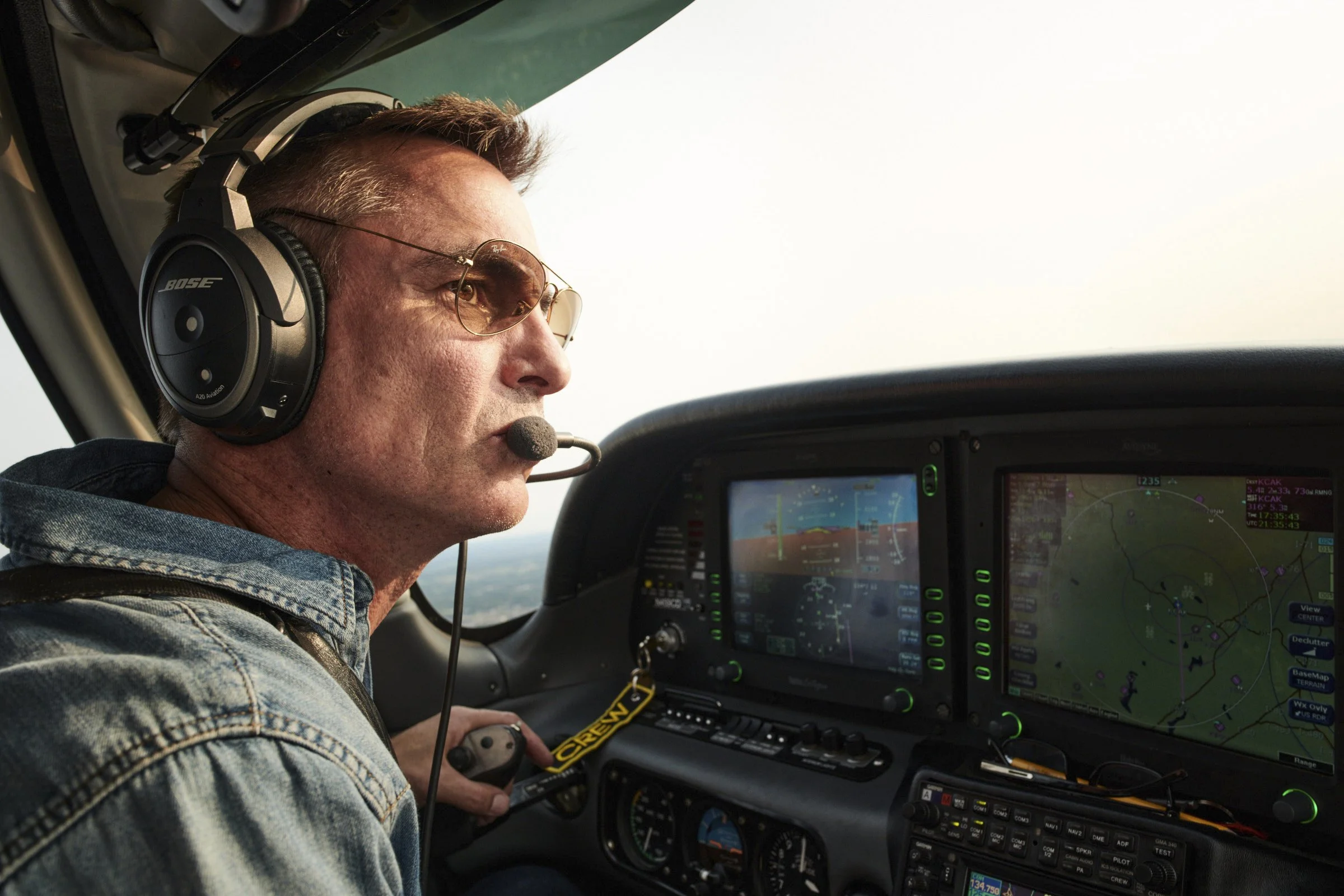 A male airplane pilot wearing sunglasses and Bose headphones, sitting in the cockpit with altitude and navigation screens.