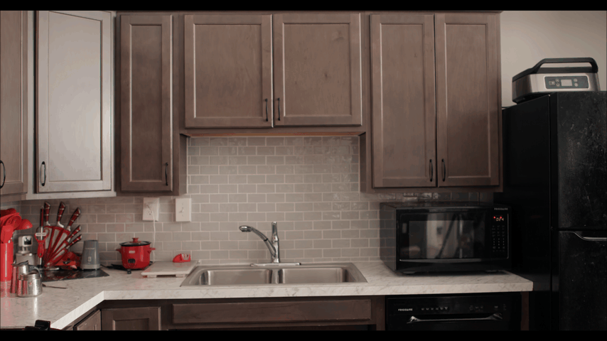Kitchen counter with wooden cabinets, a sink with a faucet, a microwave, a black refrigerator, and various kitchen utensils and appliances.