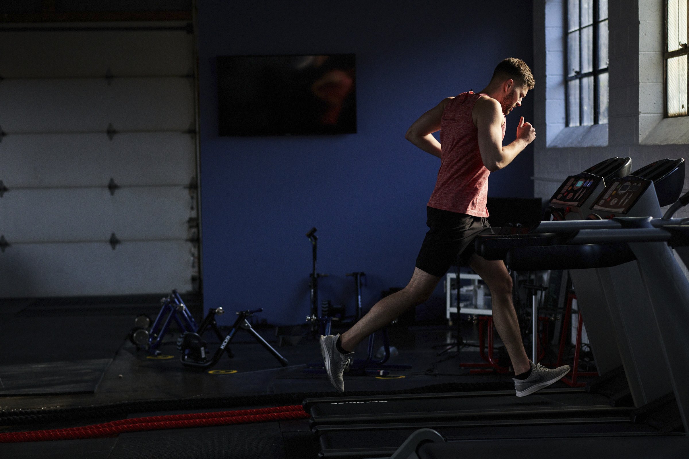 A man running on a treadmill in a gym with blue walls and a window with natural light.
