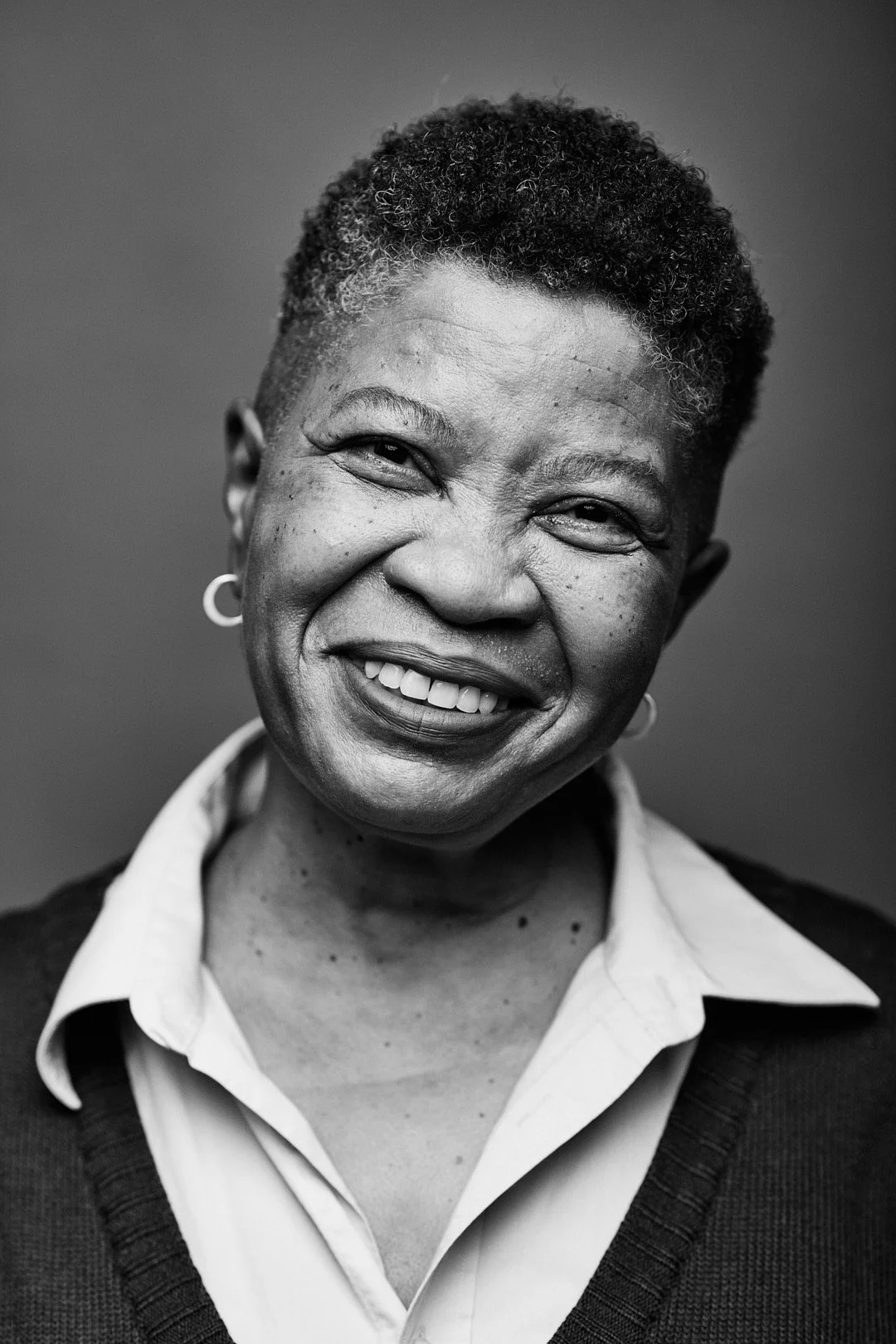 Black and white portrait of a smiling woman with short curly hair, wearing a collared shirt and a sweater.