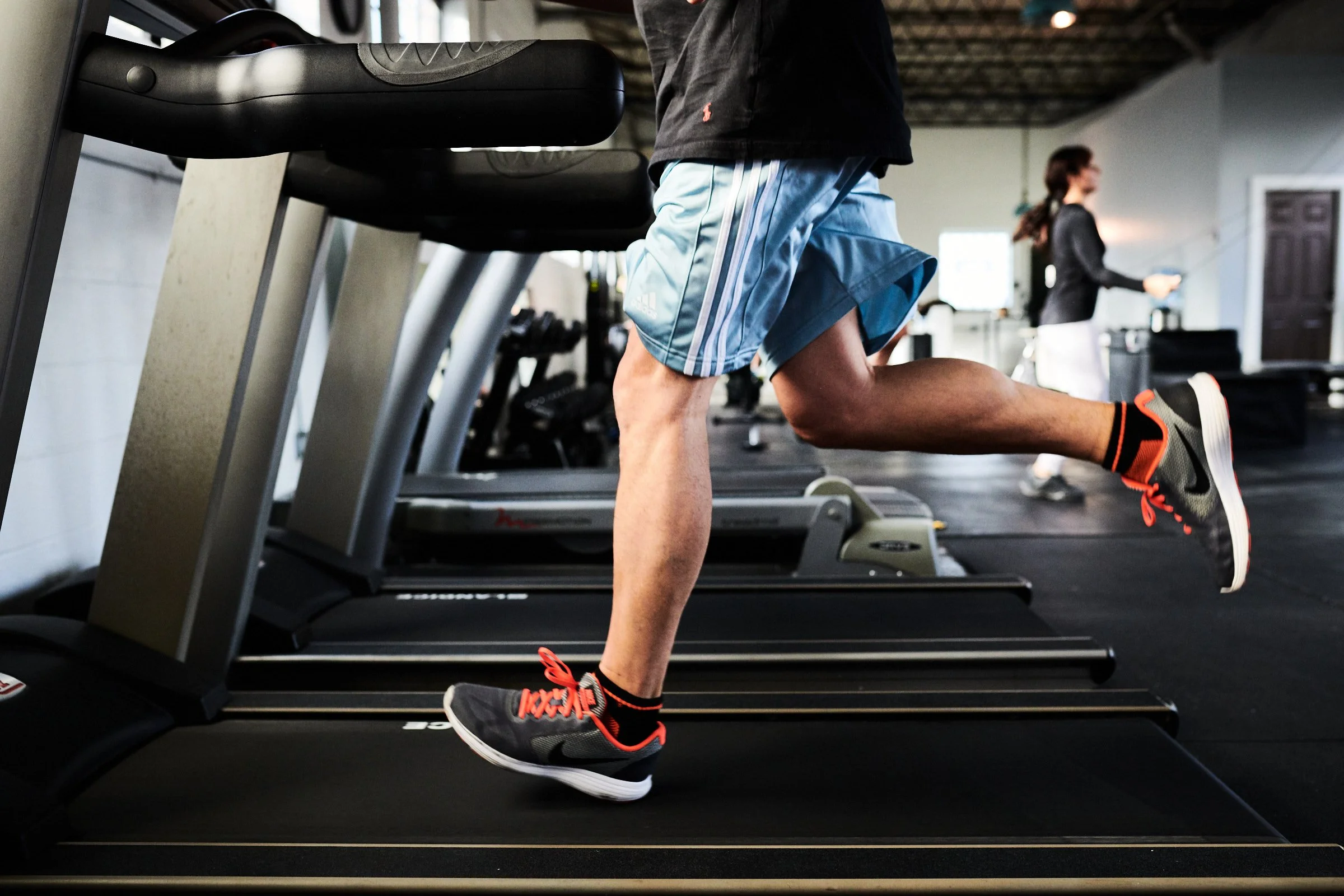 Man running on a treadmill in a gym with a woman in the background.