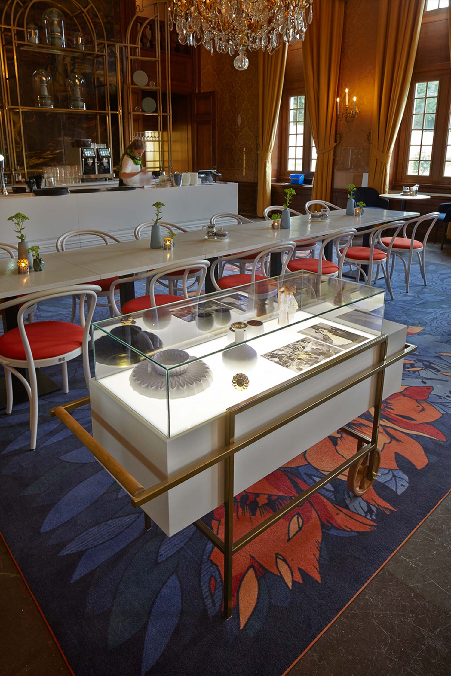 Fixed and mobile show cabinets, made in a classic wireframe structure, allow a glimpse of the historical wall leather paintings. They display glassware and artefacts belonging to the palace’s past, while custom printed-carpets in rich red and blues recall the floral beauty of its gardens. 