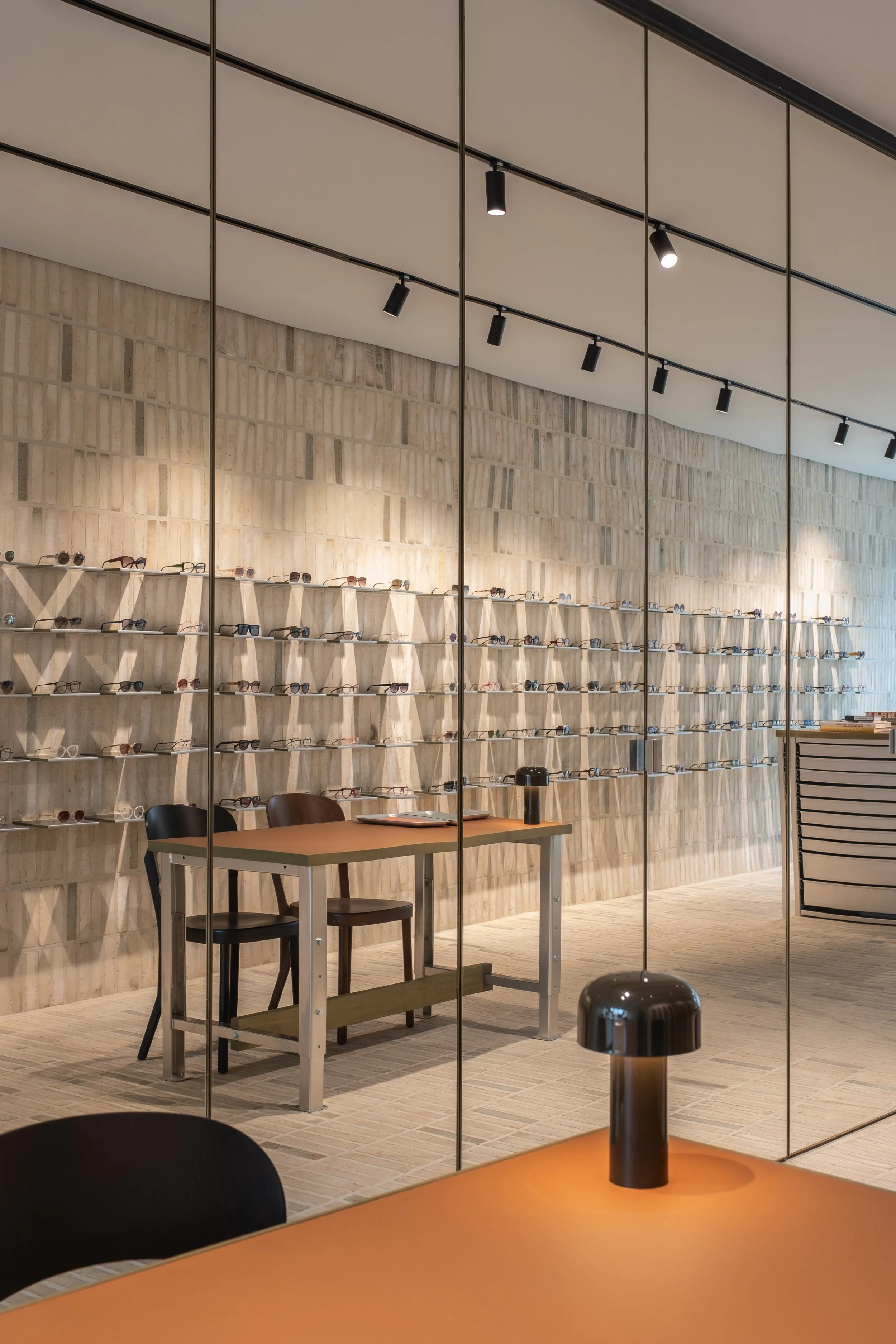  Behind the mirrored surfaces, essential functions are seamlessly integrated into the architecture. An atelier for repairs and adjustments, spaces for vision and hearing tests, storage and other supporting functions remain concealed, preserving the c