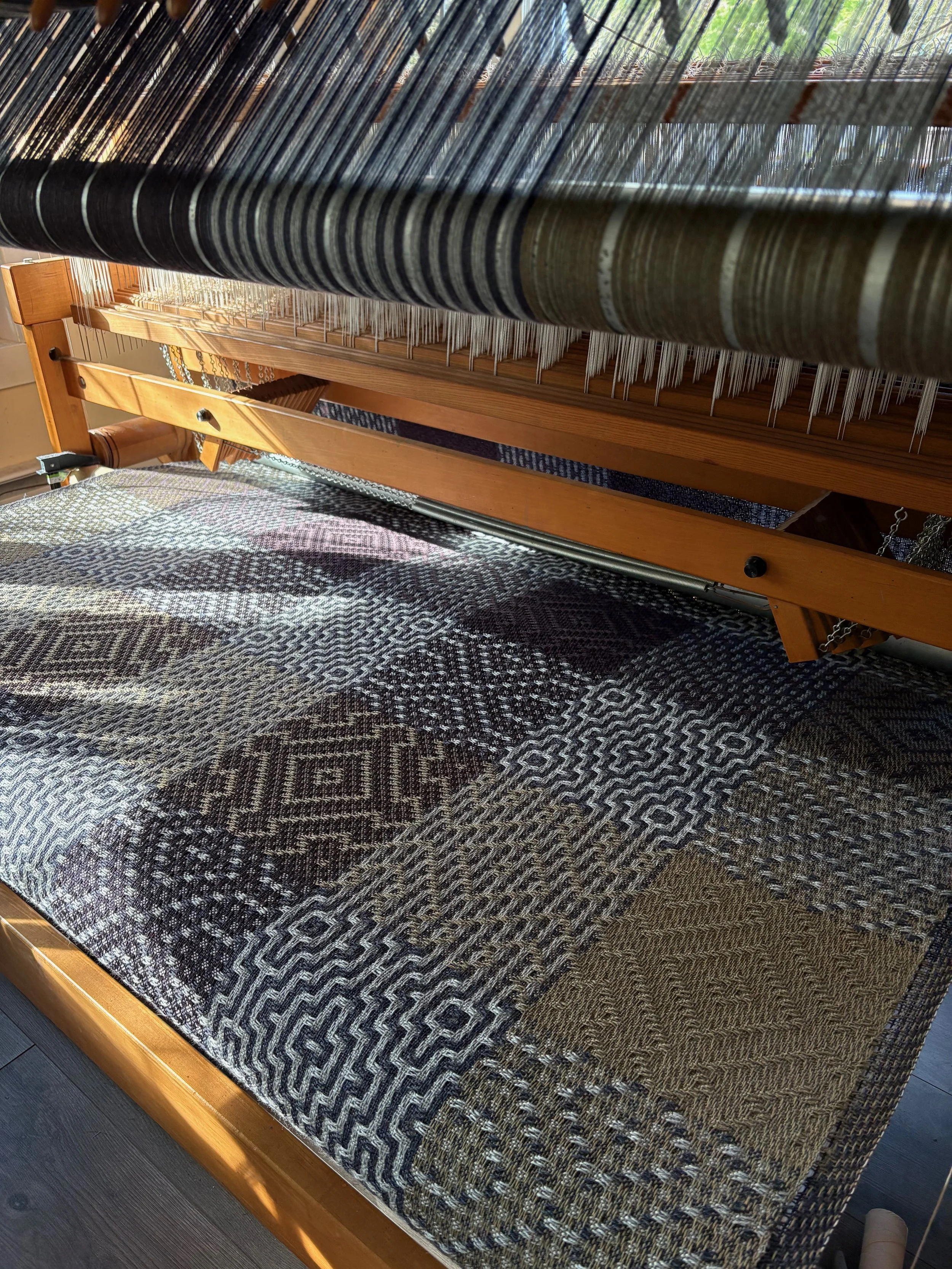 handwoven cloth on an AVL production dobby loom rolling back to the cloth storage take up.