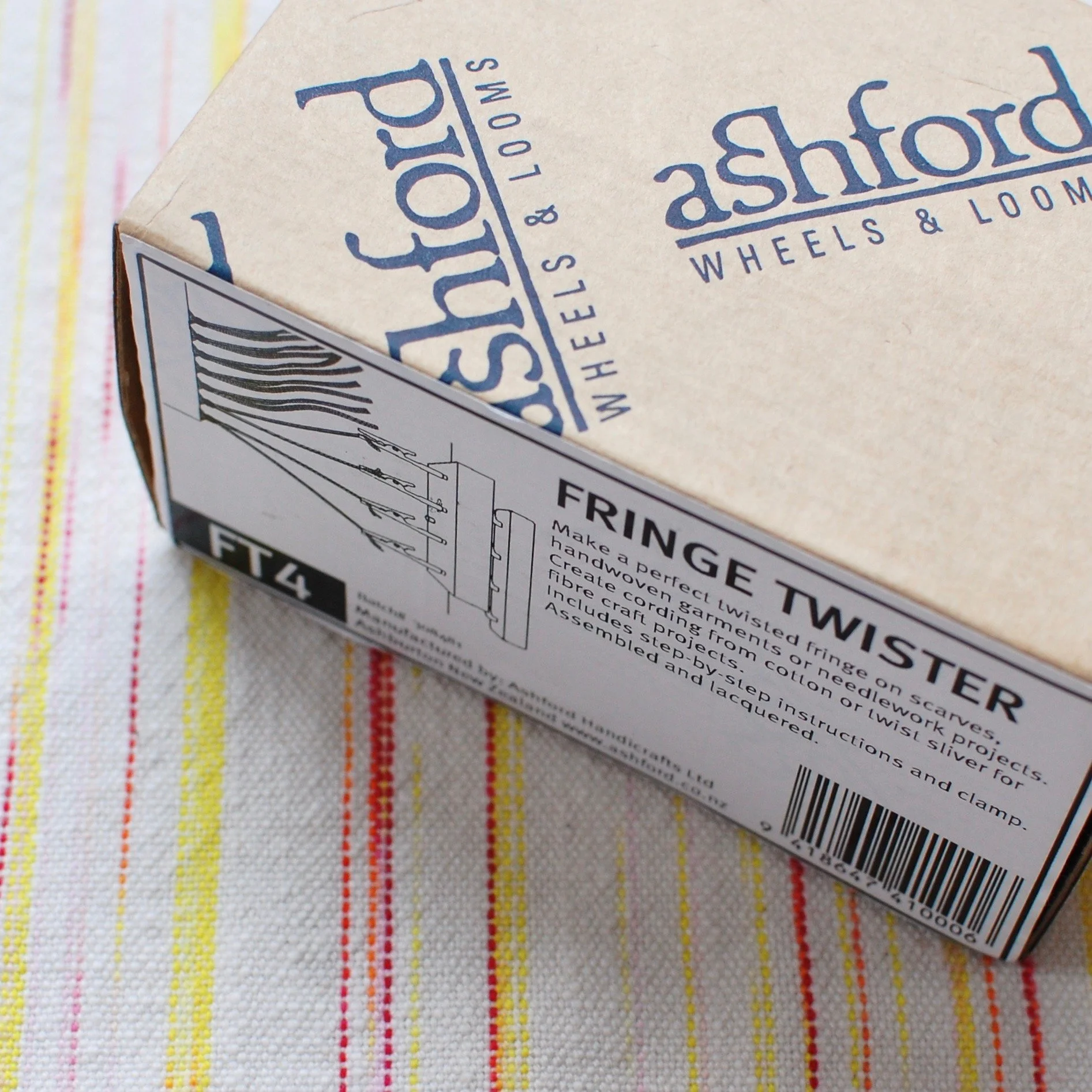 Ashford Fringe Twister in a its packaging on a handwoven textile