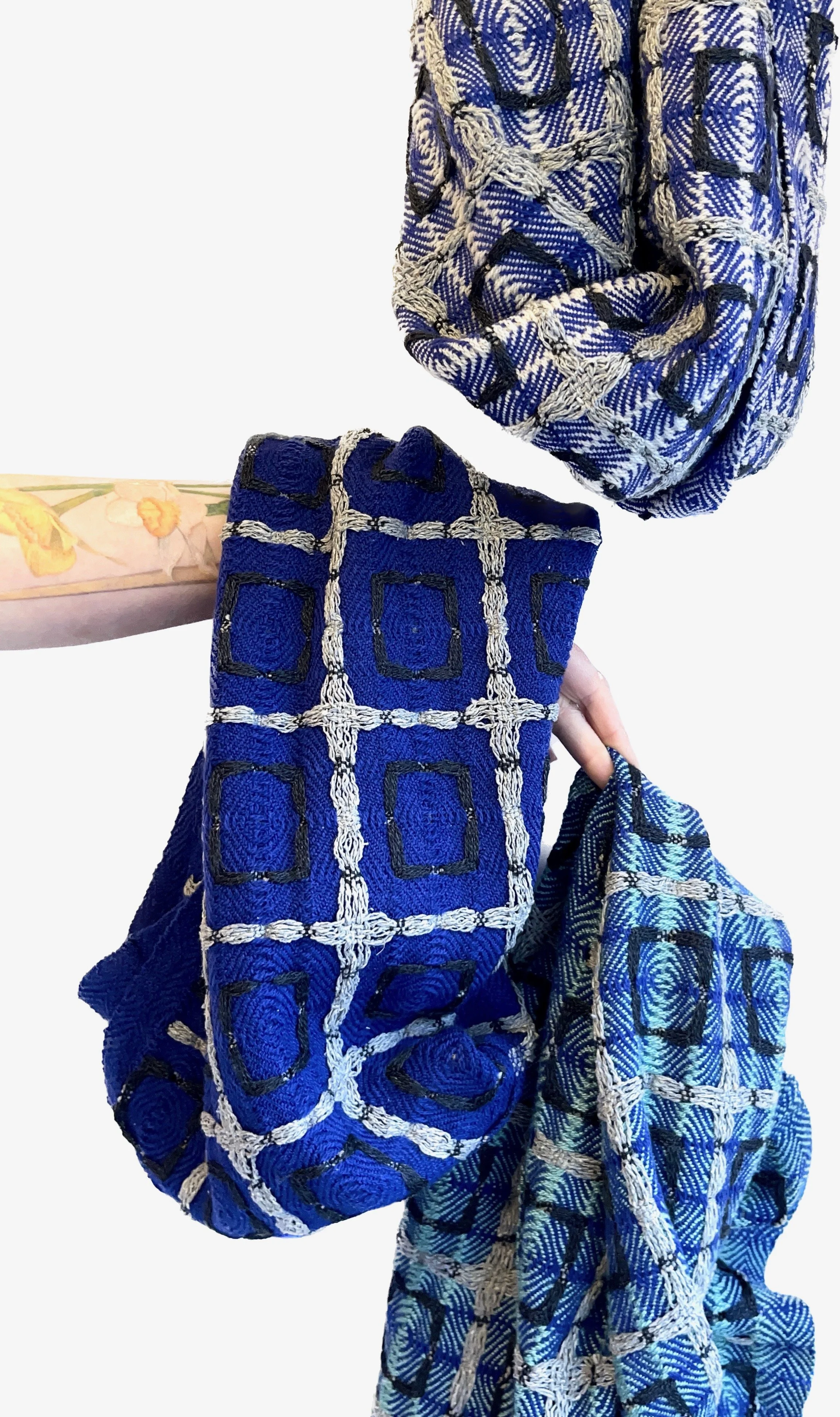 a tattooed arm with daffodils handing handwoven scarves