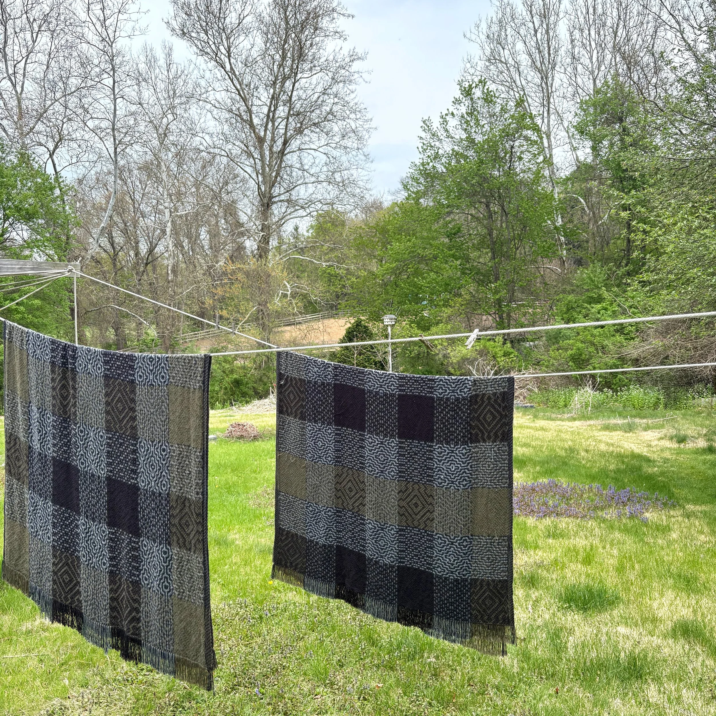 handwoven blankets drying on a clothes line with fresh spring grass.