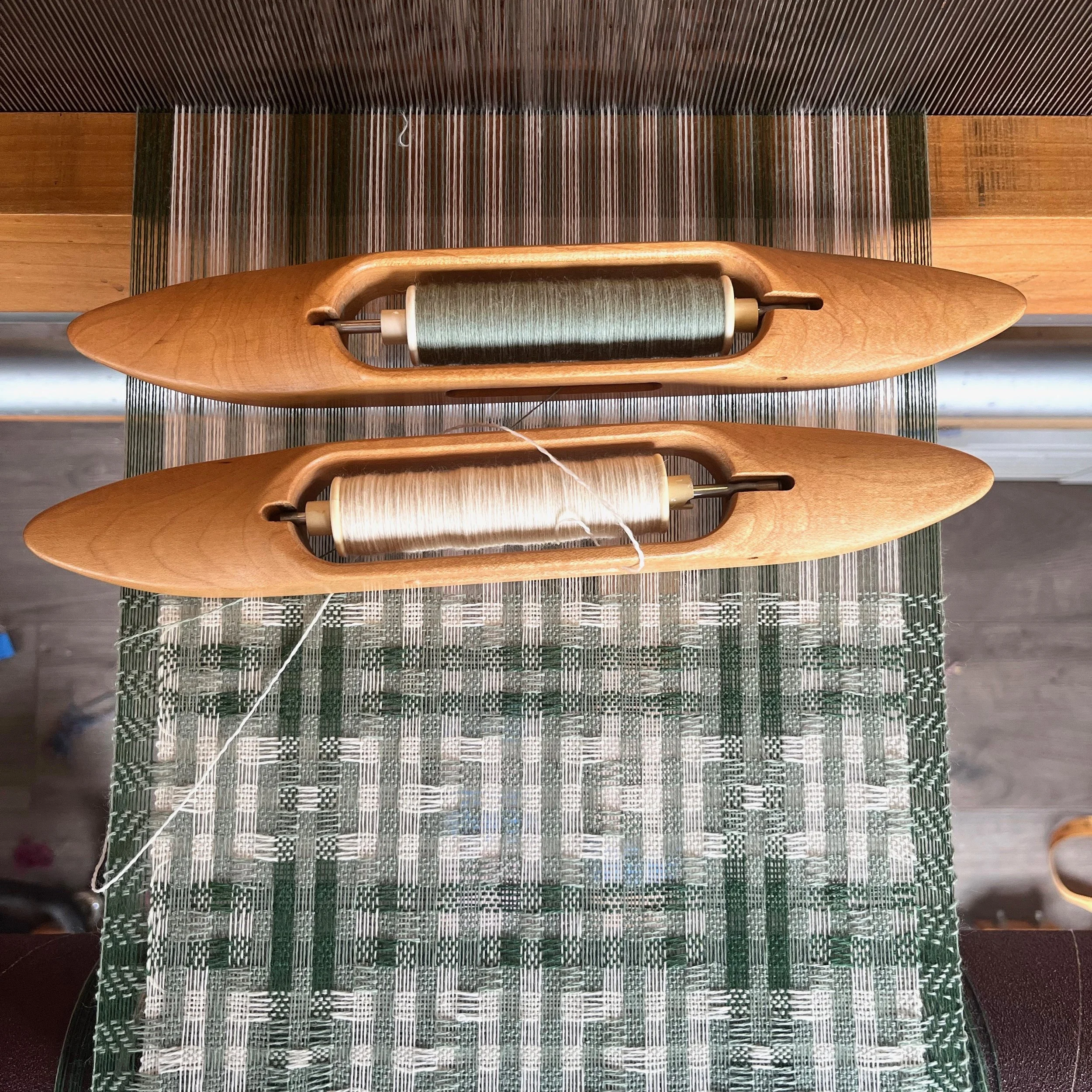 Green scarf being handwoven on a loom with two boat shuttles