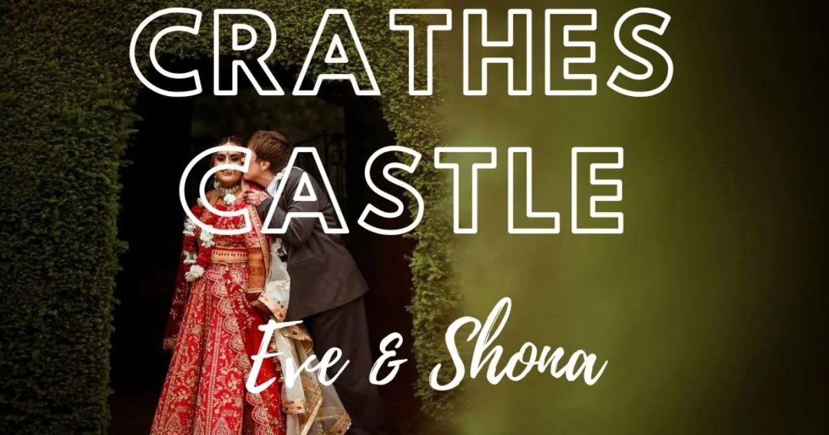 Romantic image of two same-sex brides, one in a suit and one wearing traditional Indian red dress wedding attire, kissing in the grounds of Crathes Castle.