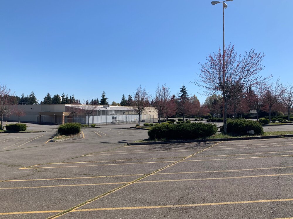 The existing site, with a large parking lot and vacant retail structure.