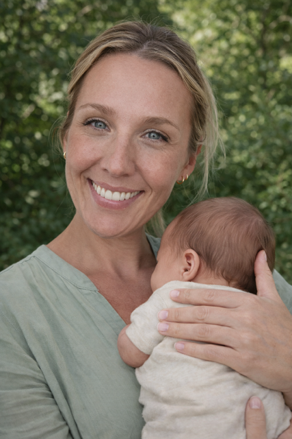 image of a smiling blond overnight doula in SW Portland holding an infant in a onesie.