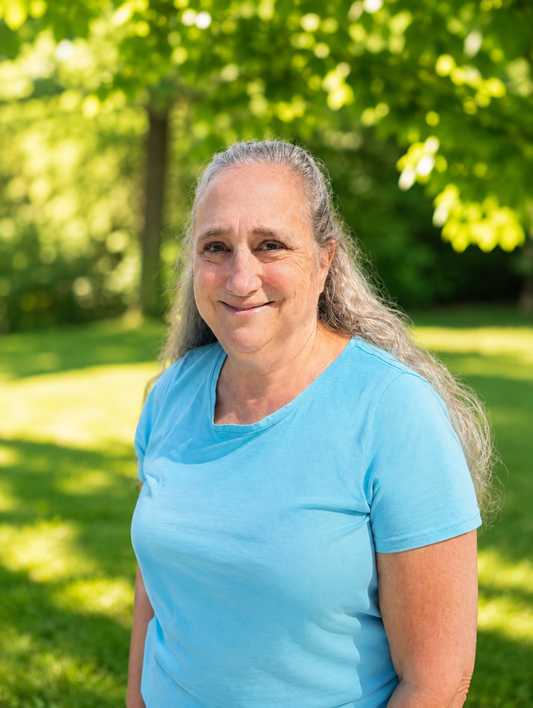 Image of a smiling silver haired doula in Beaverton, OR with a blue shirt standing against a green background just outside of Portland, OR.