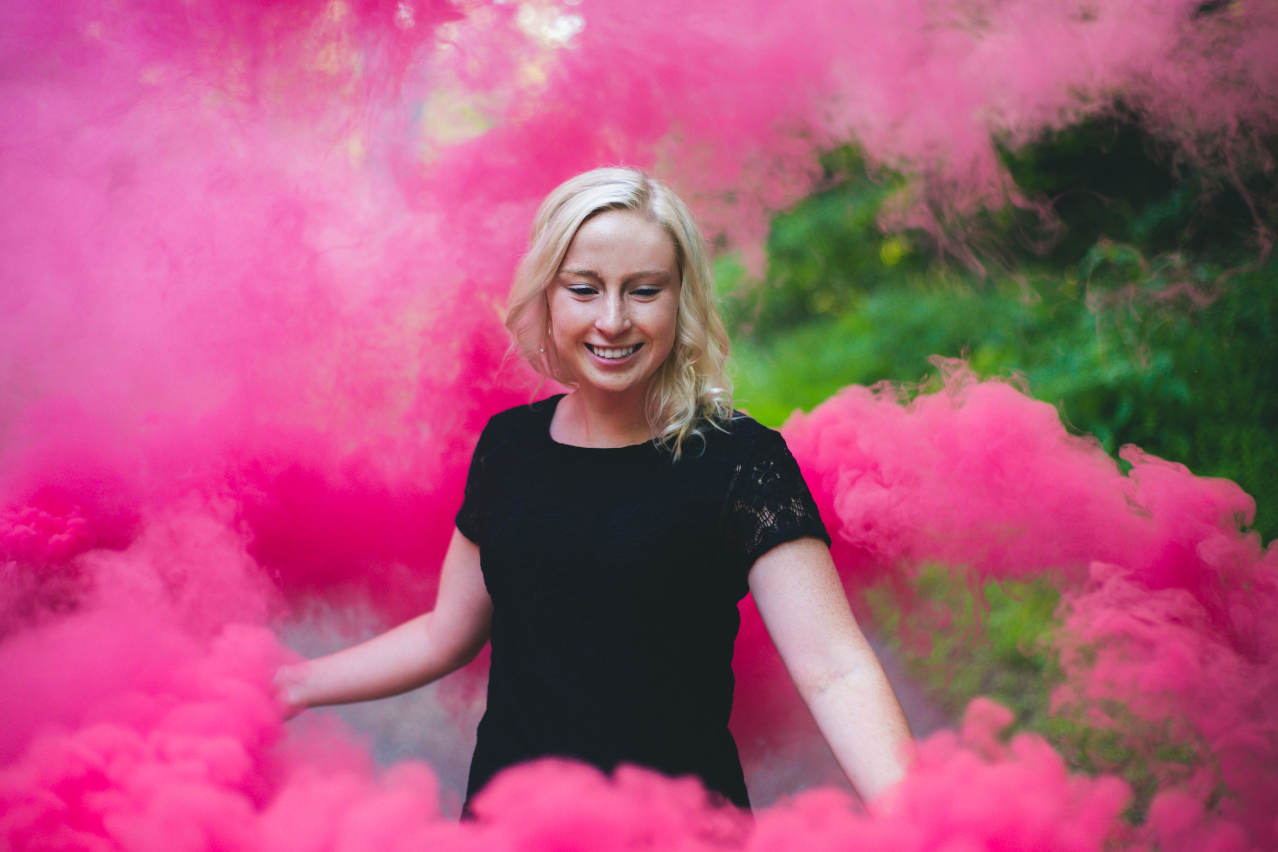 Pink smoke bombs surround blonde smiling high school senior