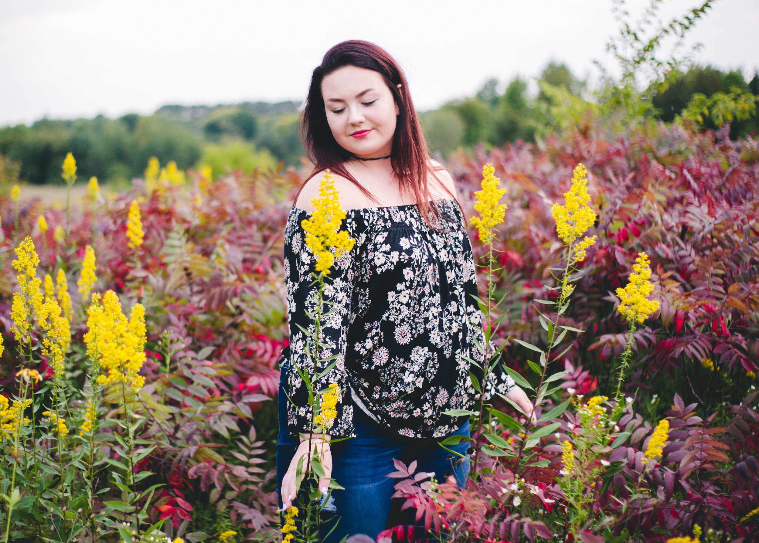 Yellow and red plants in meadow surround high school senior in Hudson WI