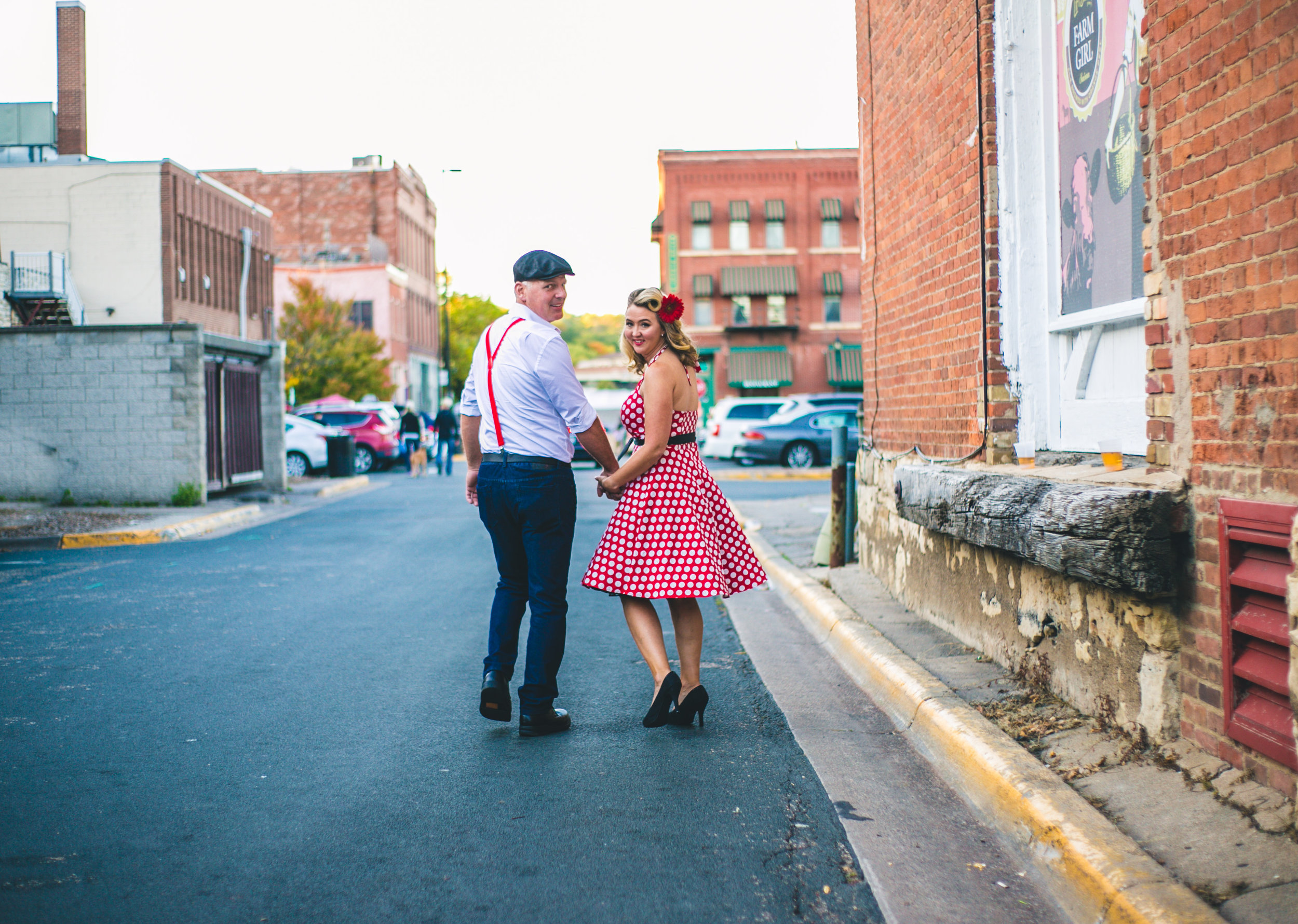 Vintage travel-inspired engaged couple walk down the alley of Stillwater MN