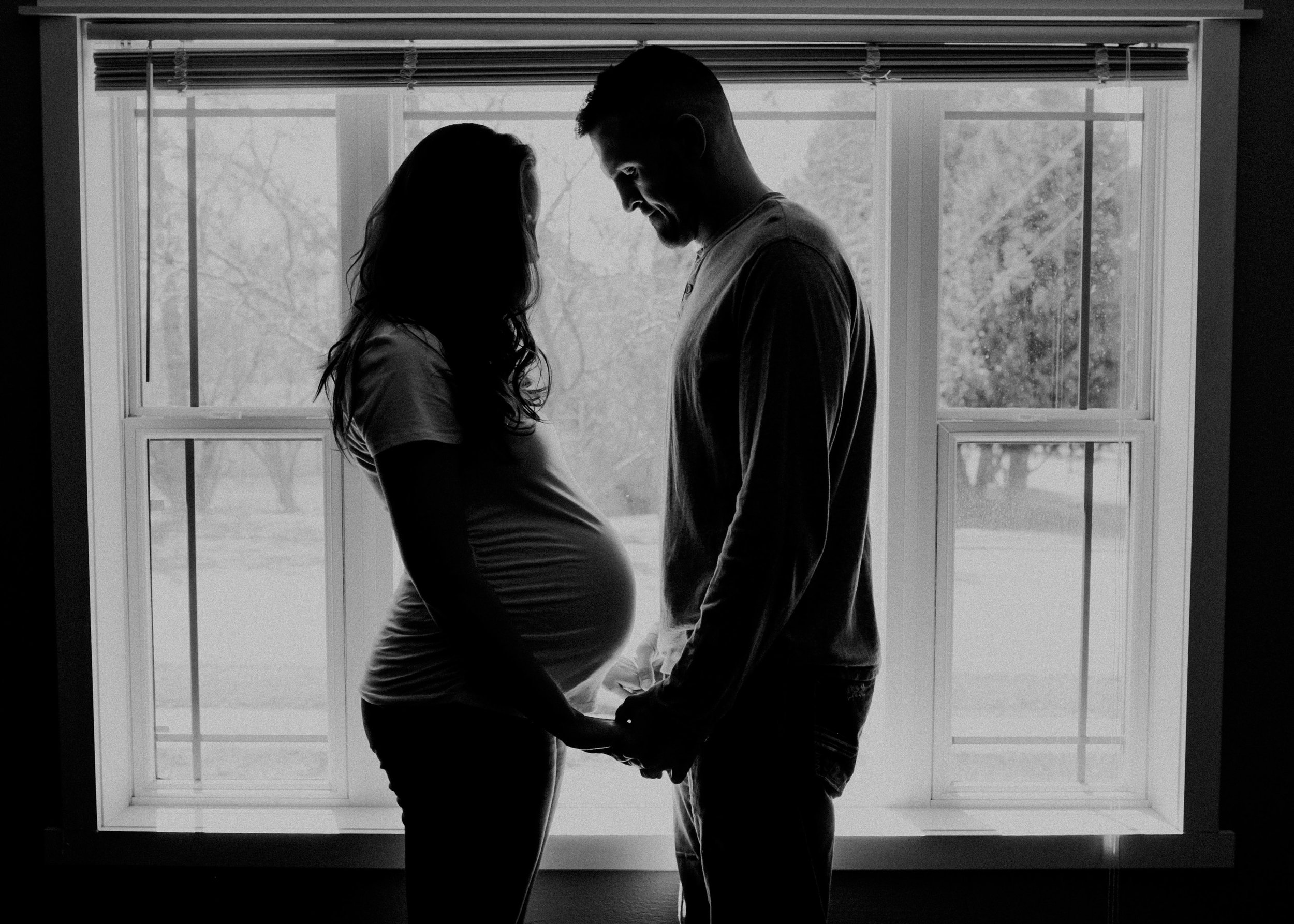 black and white photo of man and woman looking at belly expecting baby