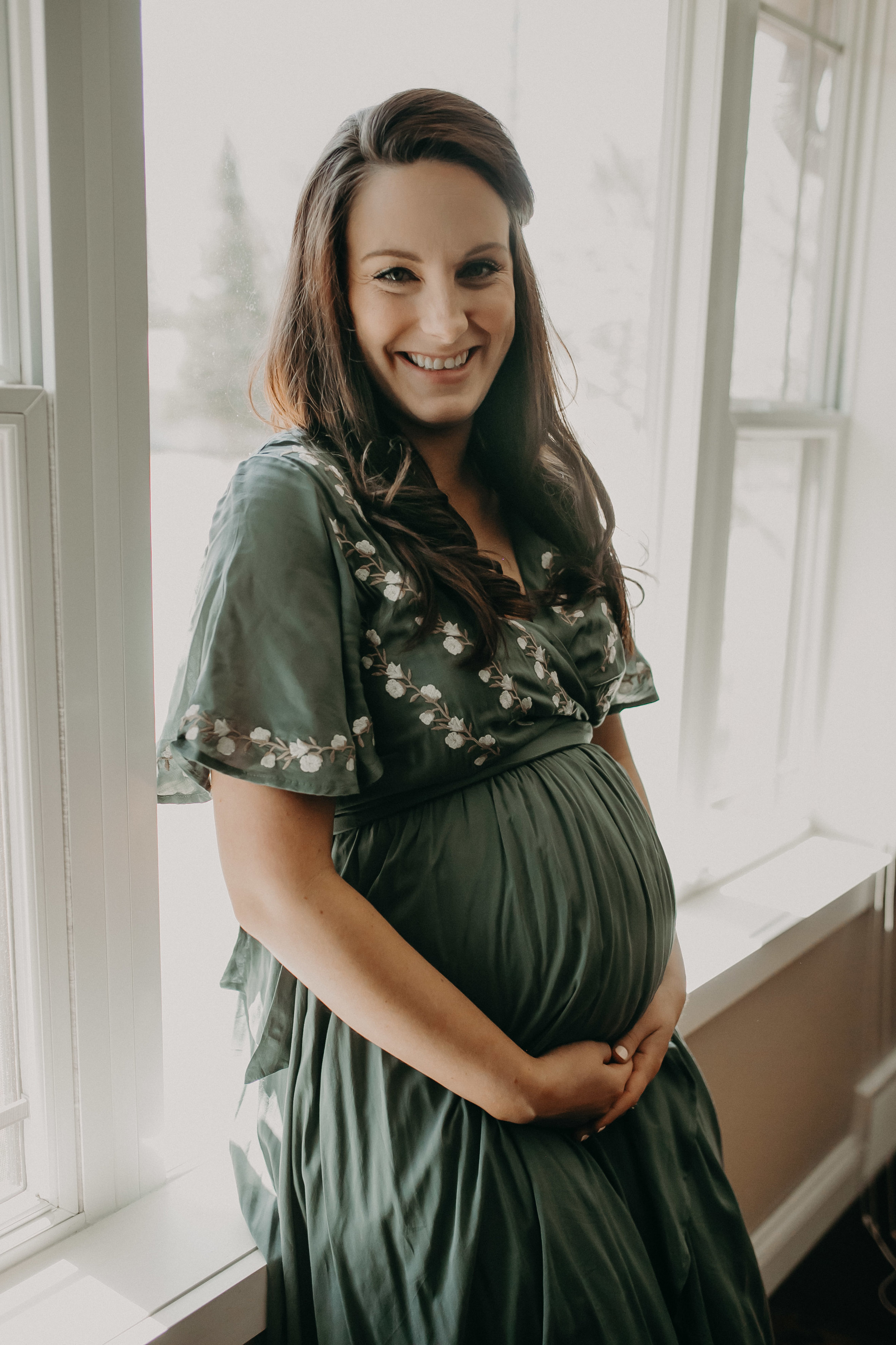 pregnant woman smiling in teal dress in front of window