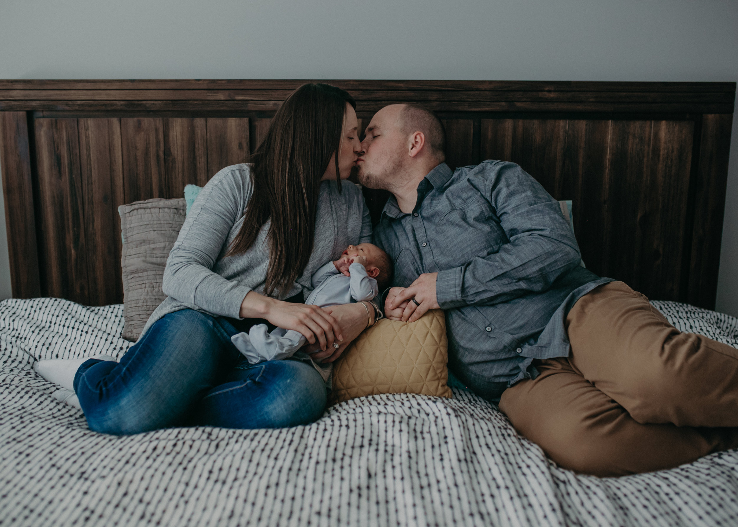  Chaska MN family kissing on bed holding newborn baby 
