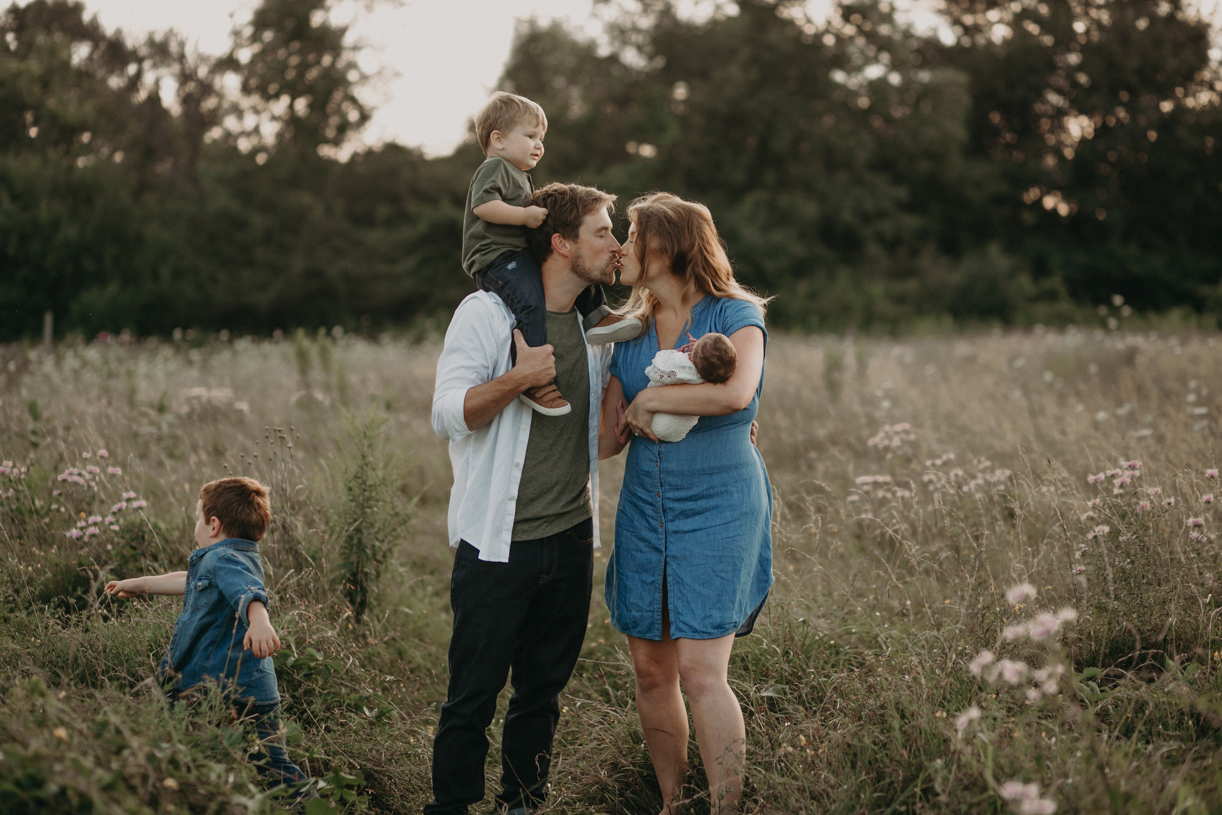  Mom and dad kissing in field in River Falls WI while toddler runs 