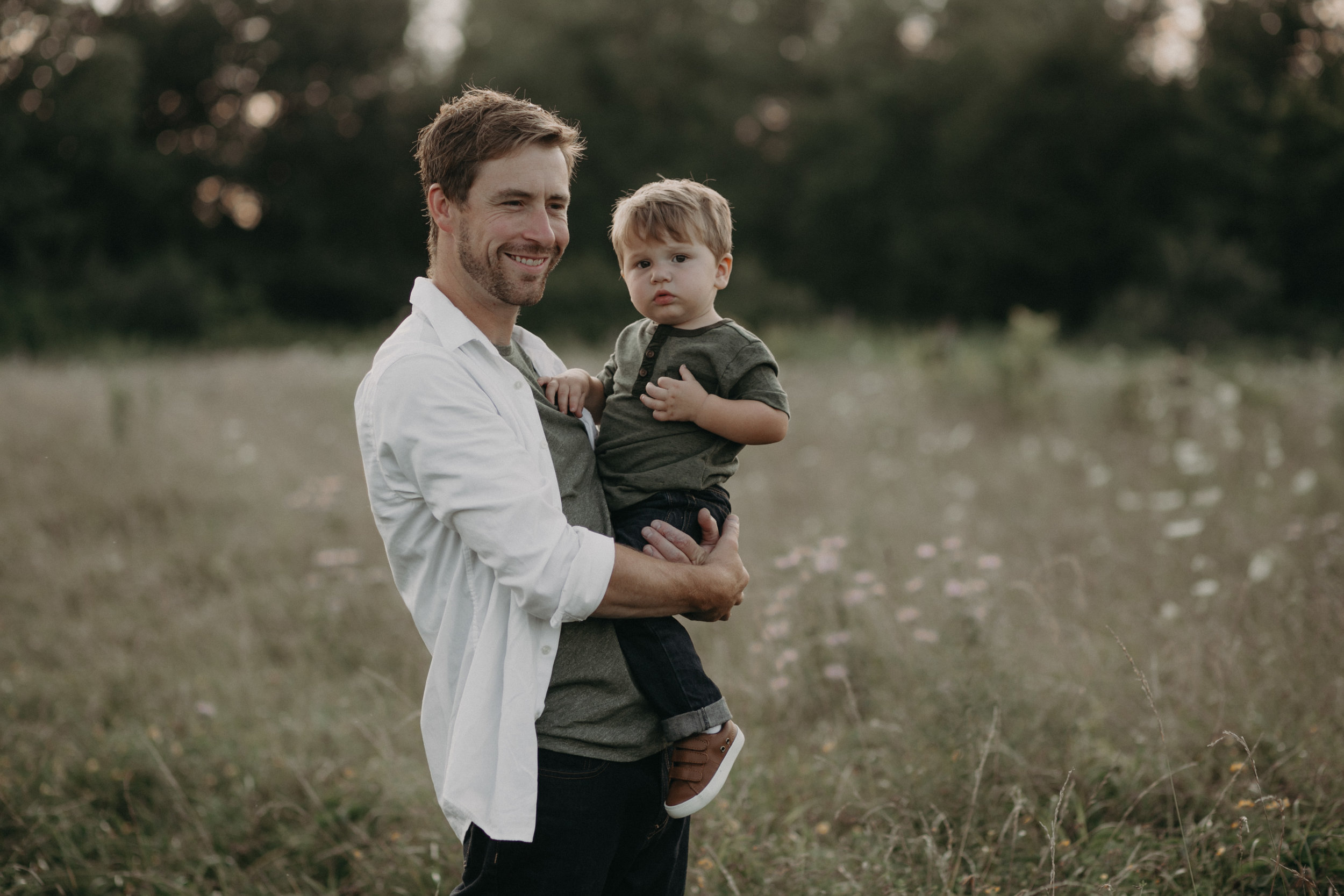  Daddy holding toddler son and smiling in field 