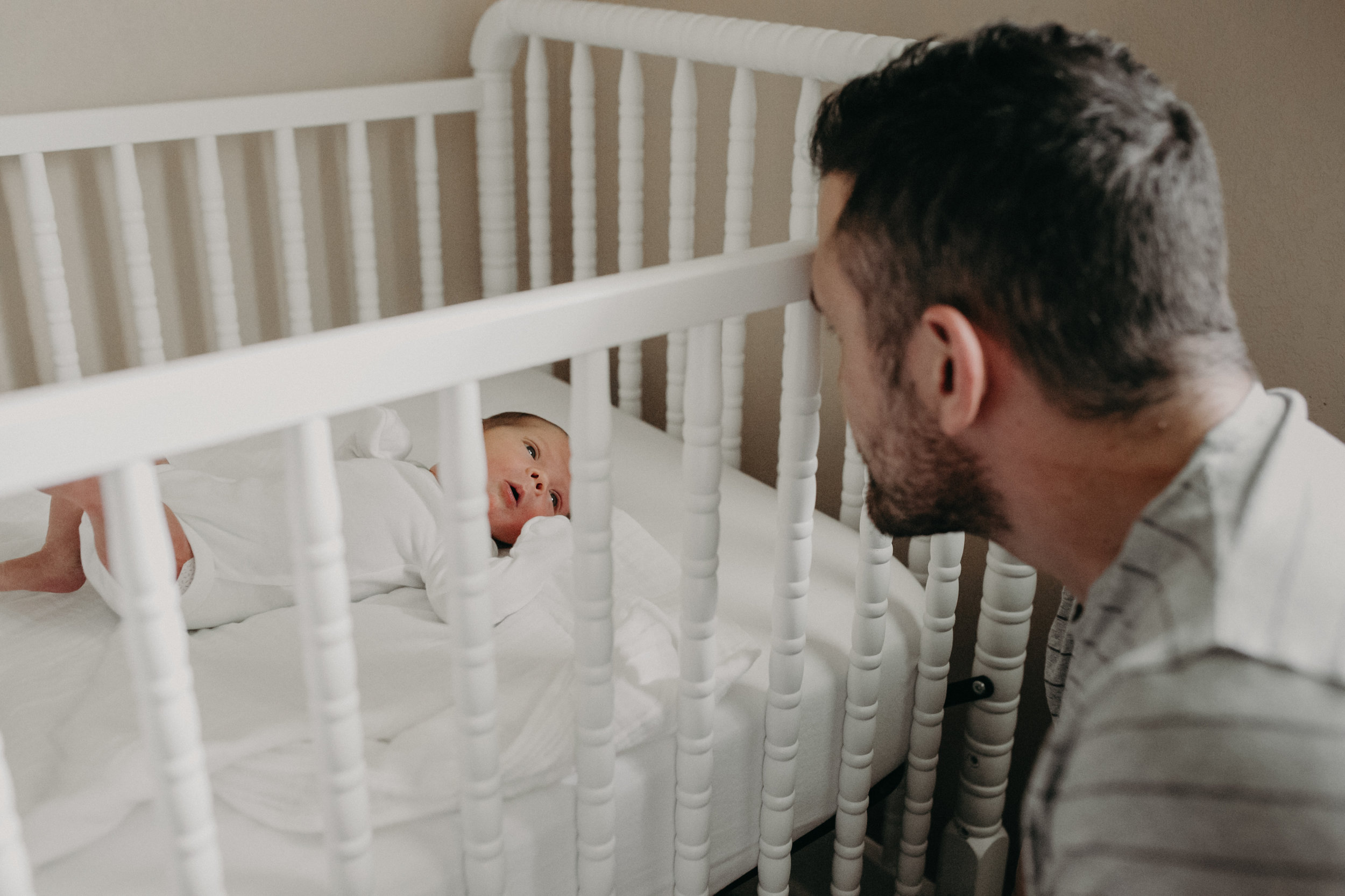  new dad looking at newborn baby in white crib  