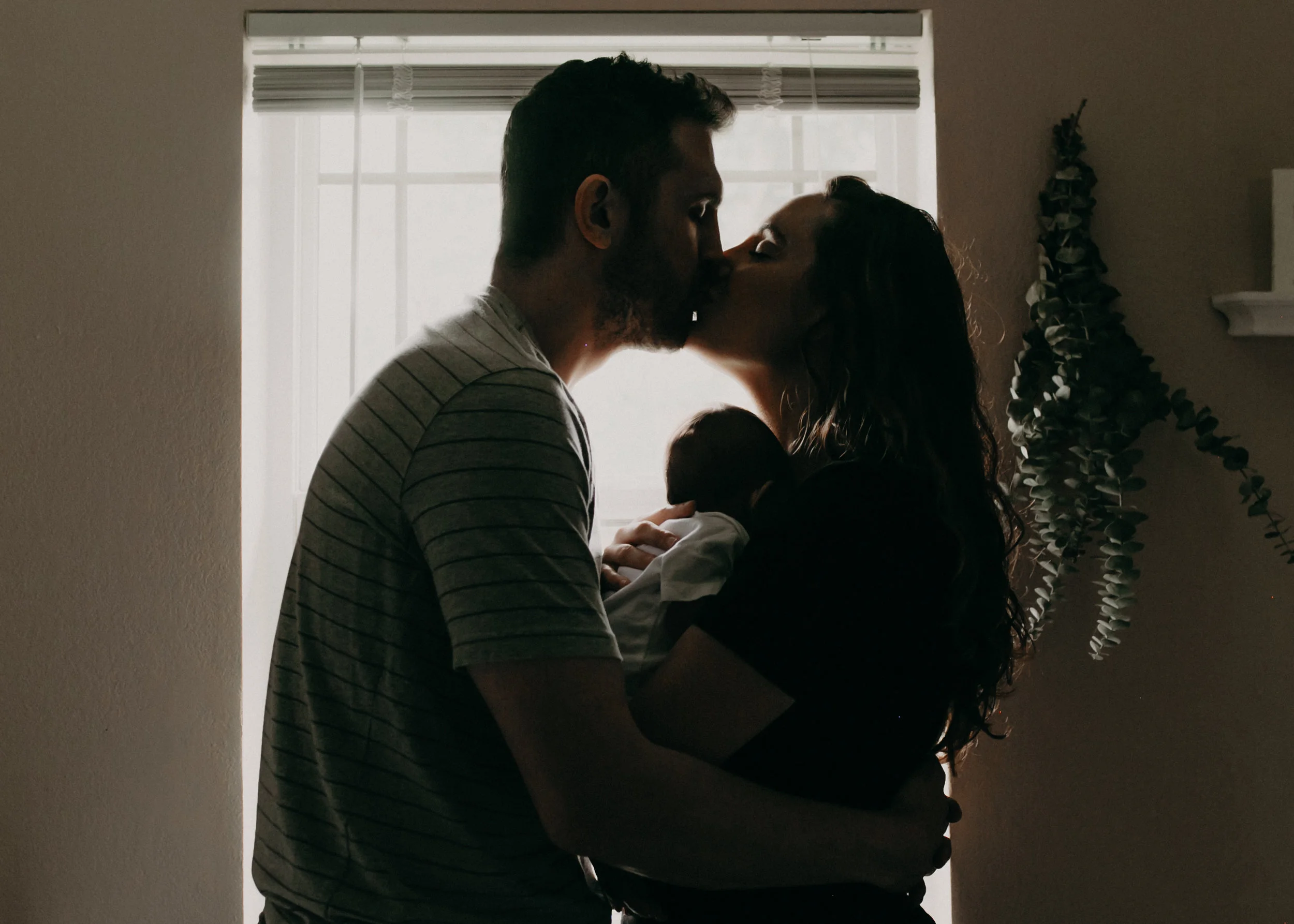 new parents in window kissing while holding newborn baby in Marshfield WI